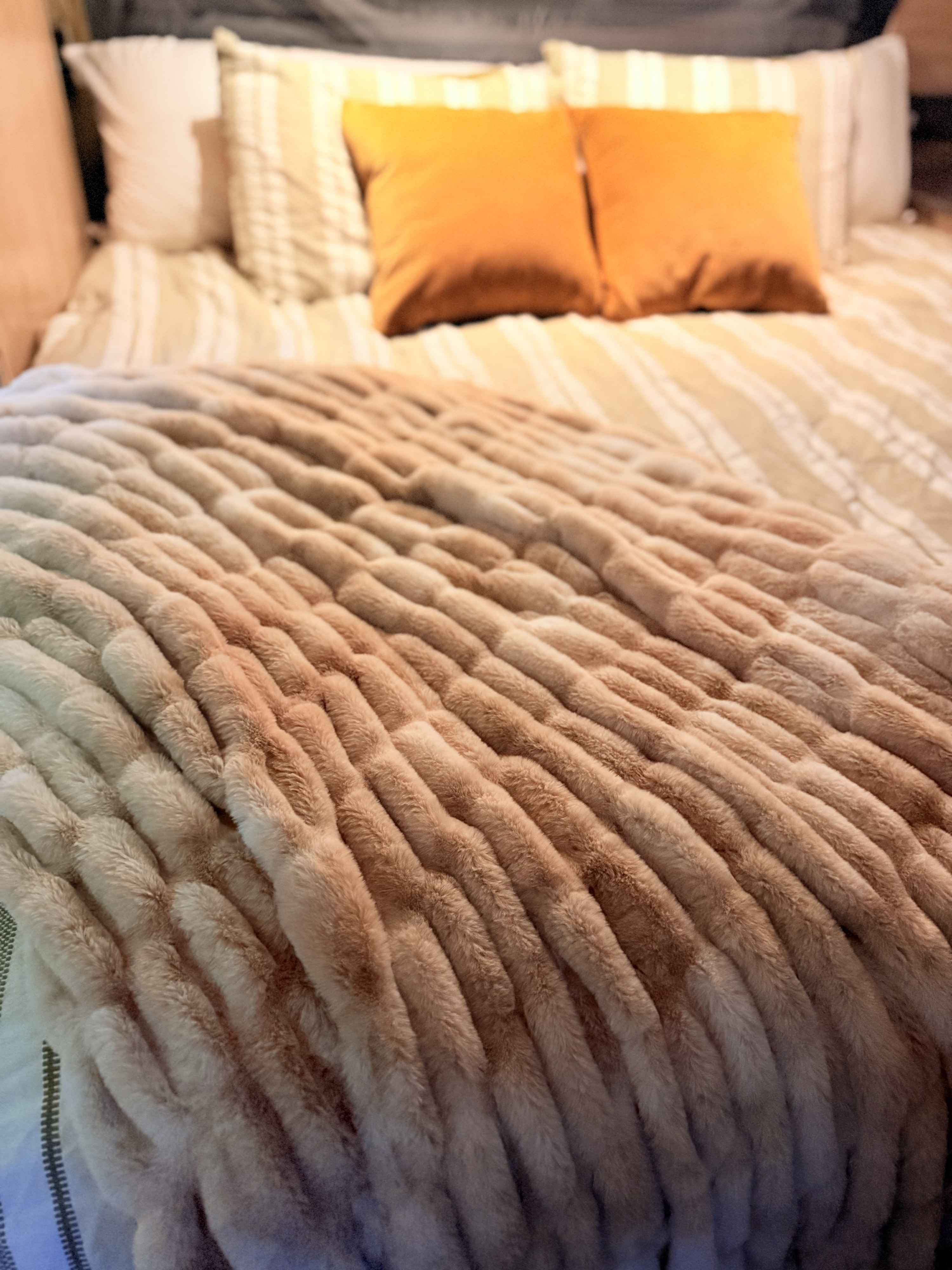 Luxurious textured blanket on a cozy RV rental bed, with striped bedding & plush orange pillows for comfortable travel.. Forest River Campsite Reserve 2026
