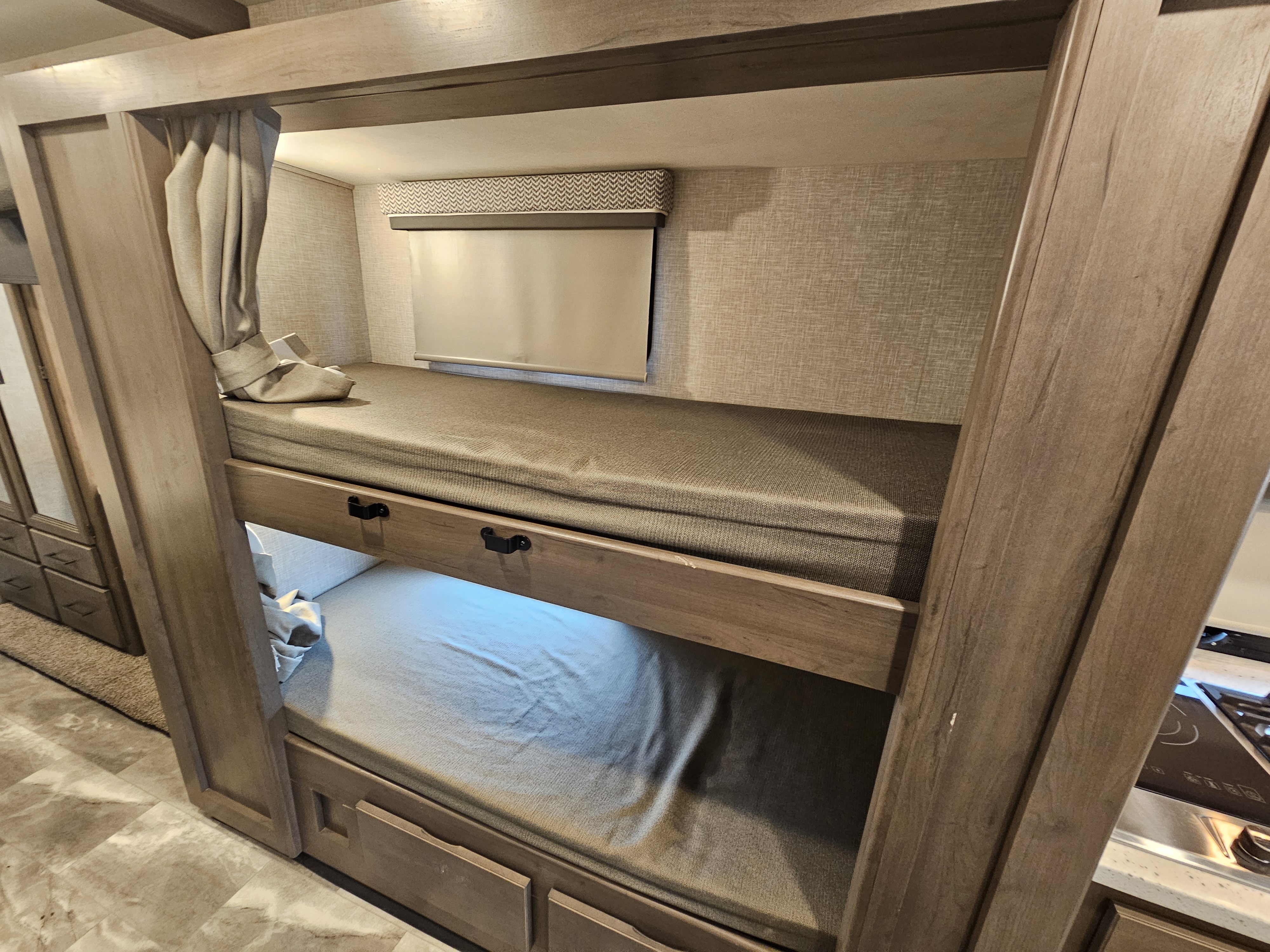 Compact RV rental sleeping area with wooden bunk beds, a window blind, privacy curtain, & built-in storage.. Thor Quantum 2023