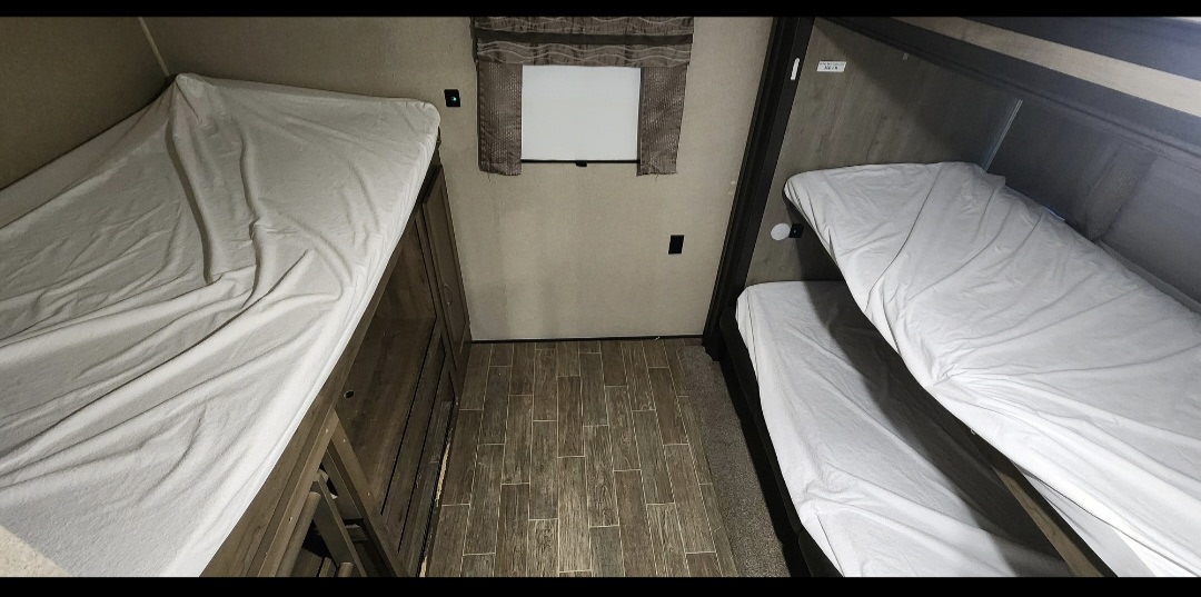Inside this RV rental, dual bunk beds with white sheets line both sides. A wood-look floor and small window complete the compact sleeping space.. Forest River Palomino Puma 2020