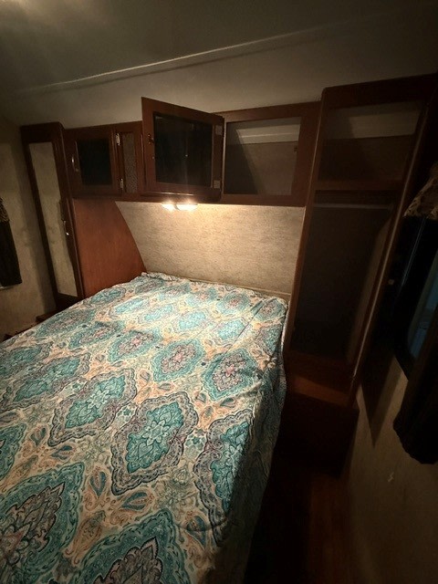 RV rental bedroom featuring a bed with a vibrant patterned comforter, overhead cabinets, and built-in storage.. Keystone RV Passport Grand Touring 2015