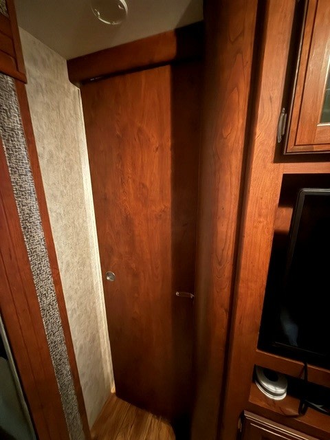 RV rental interior featuring a sliding wood closet door, integrated TV, and storage cabinets. Compact and functional design.. Keystone RV Passport Grand Touring 2015