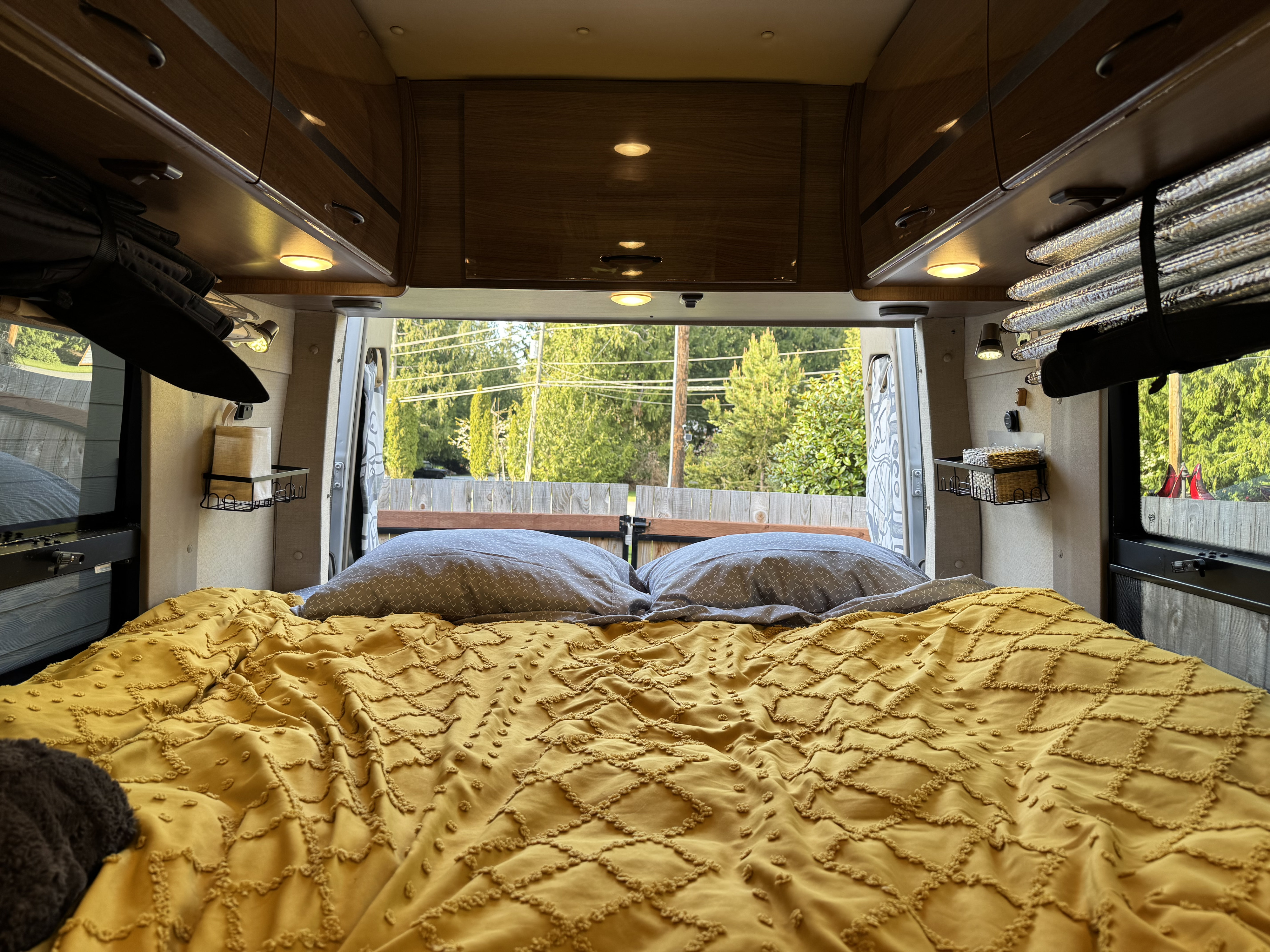 This RV rental features a cozy bed with a yellow textured comforter & gray pillows, offering a scenic view out the back.. ERA ERA Class B 2015