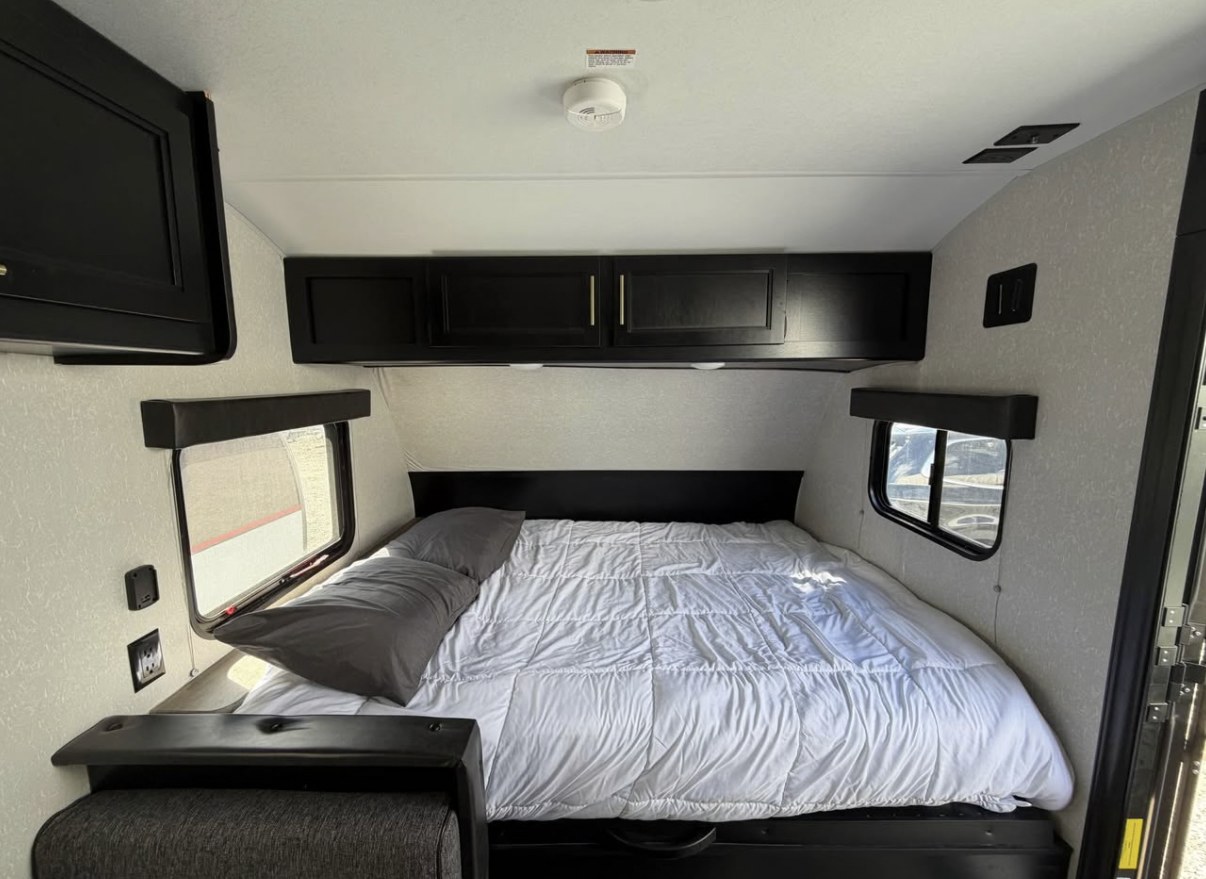 Modern RV rental bedroom with white bedding, black cabinets, and side windows, ready for travel adventures.. Forest River Cherokee Wolf Pup 2021