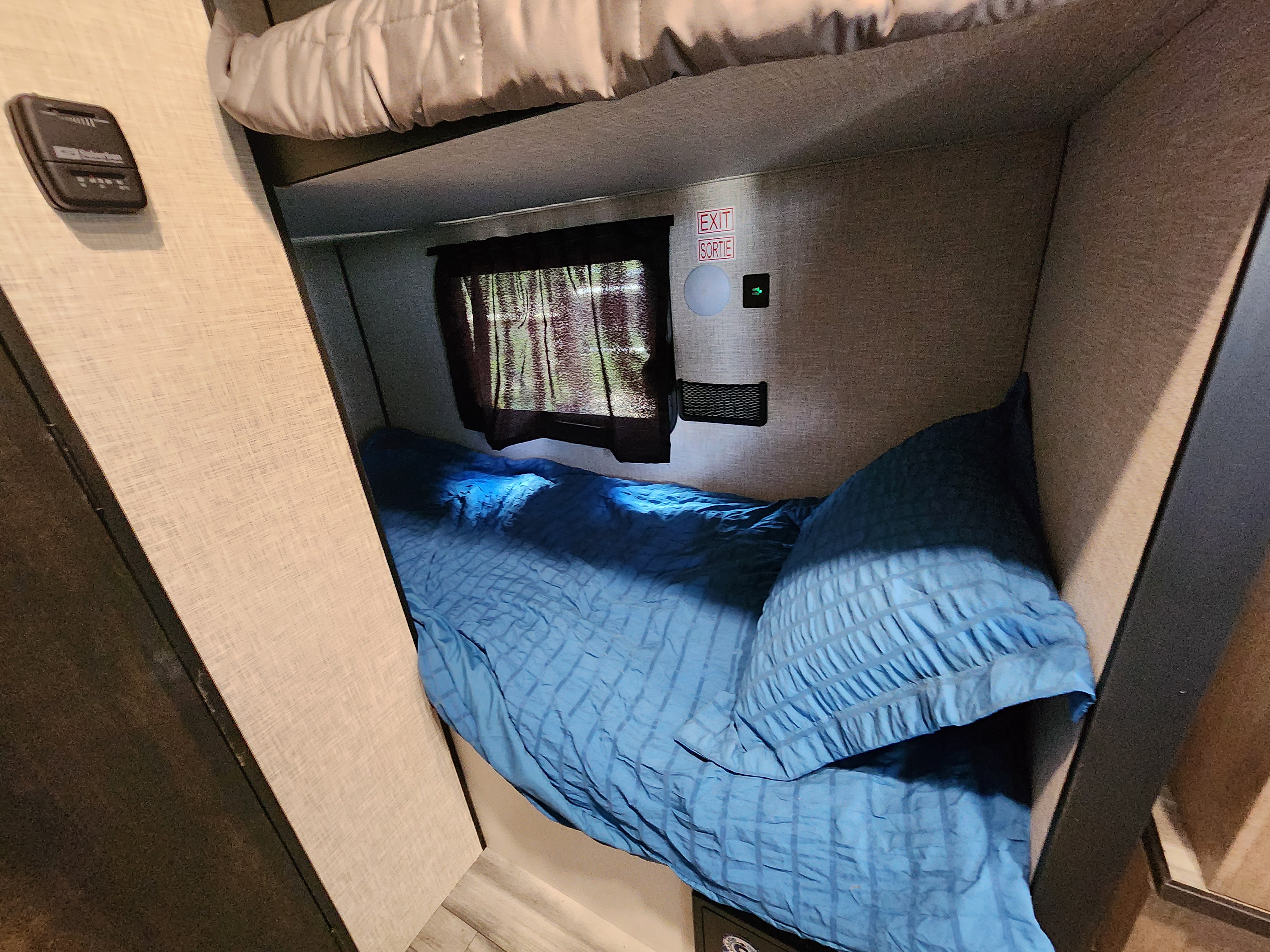 Cozy rv rental bunk bed with blue bedding, a window, and control panel, offering a compact sleeping space in an RV.. Highland Ridge RV Open Range 2024