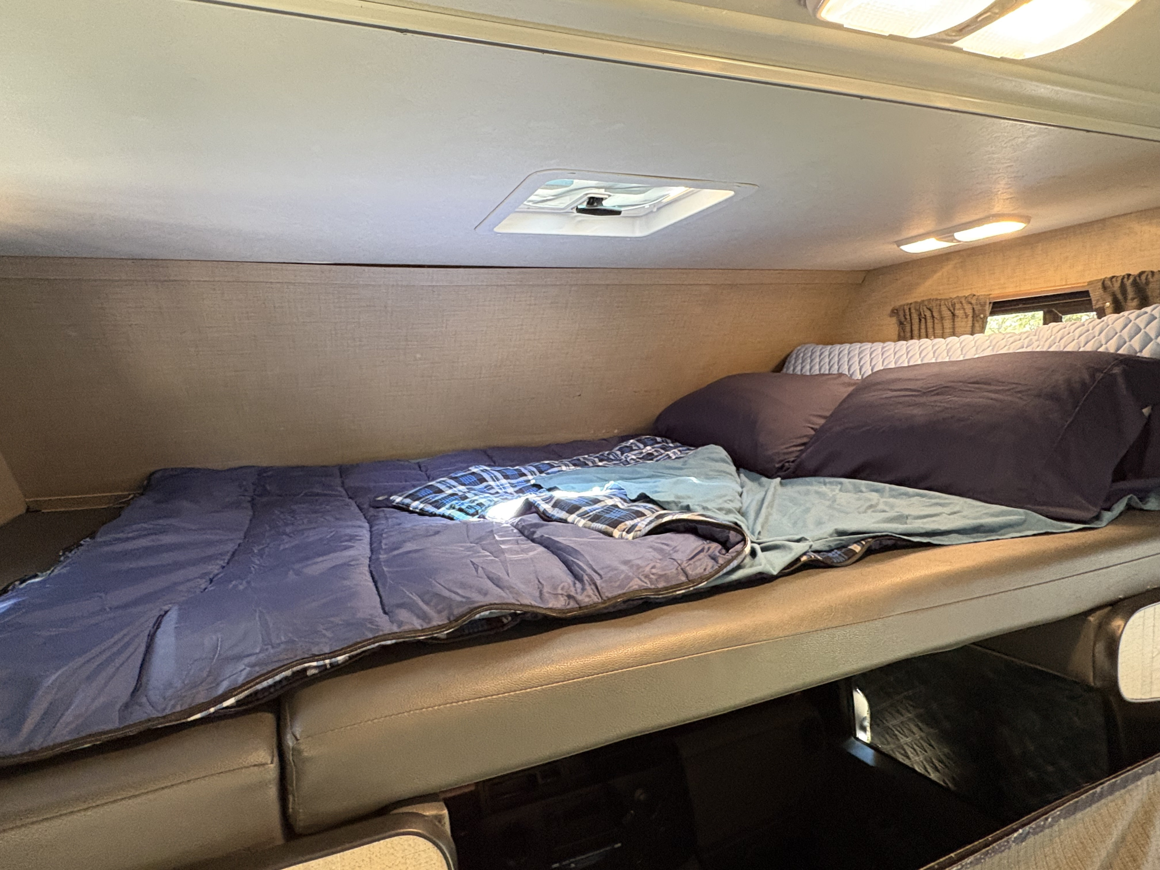 Cozy RV rental sleeping area with a bed, blue bedding, pillows, and overhead lights.. Tiffin Adventure 2020