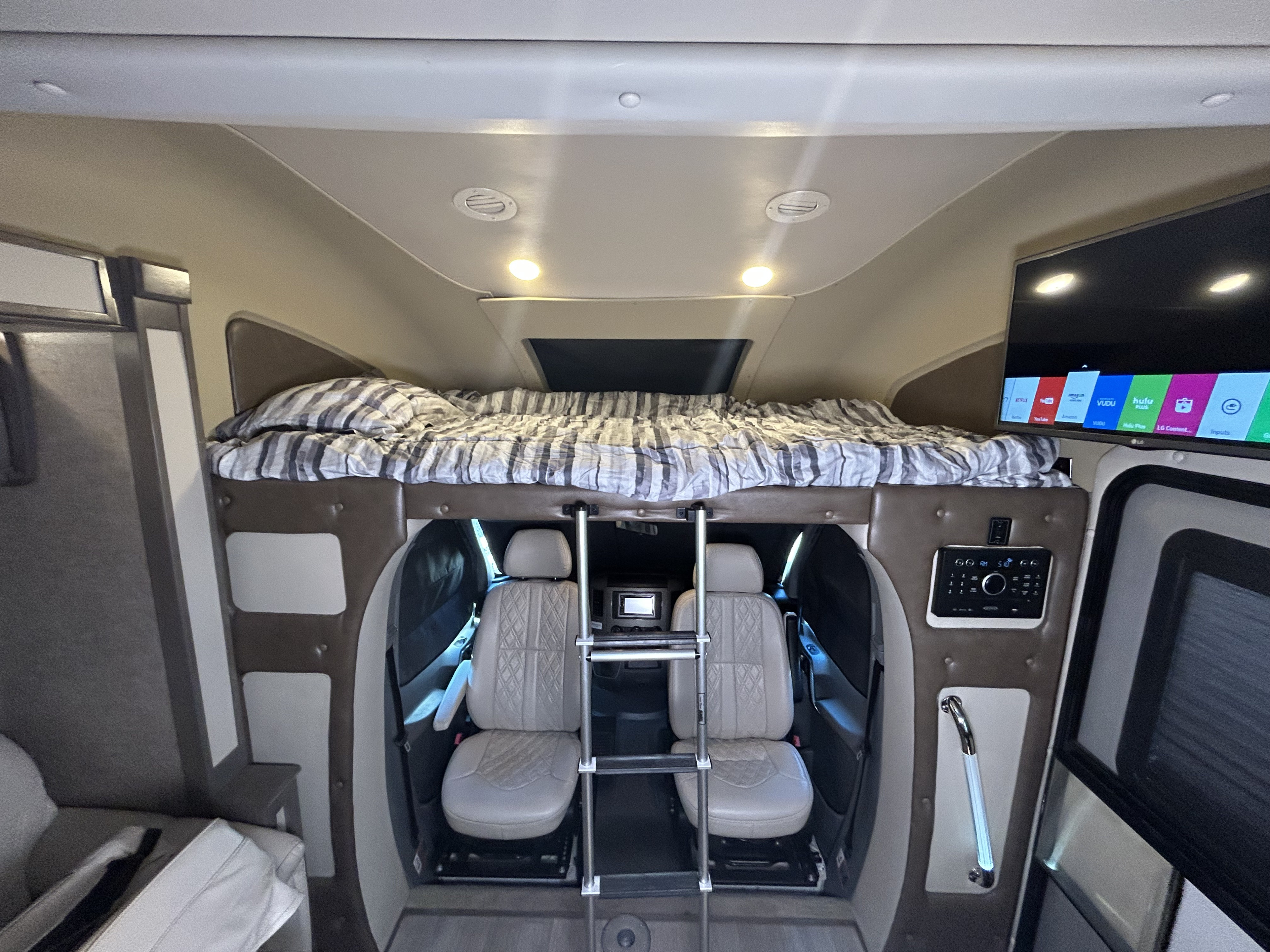 RV rental interior shows front cabin with cozy overhead bunk bed, driver/passenger seats, TV, and control panel.. Tiffin Wayfarer 2017