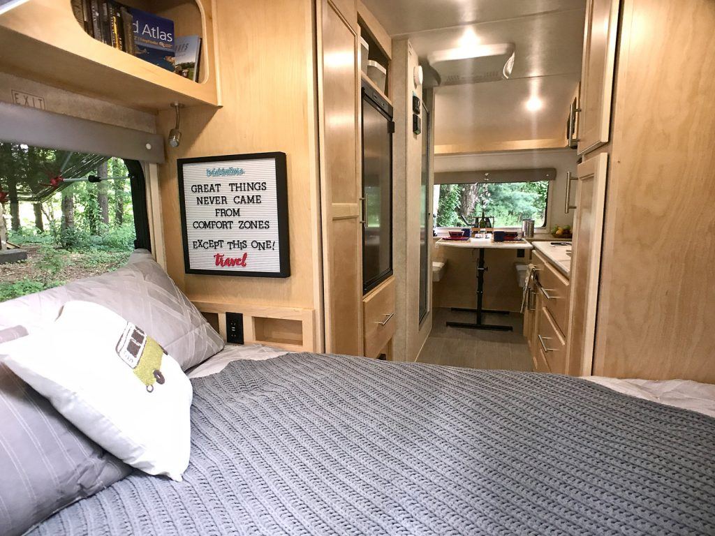 Cozy RV rental interior with a comfy bed, kitchen, and scenic window view. A "travel" quote adds inspiration.. Liberty Outdoors Little Guy 2018
