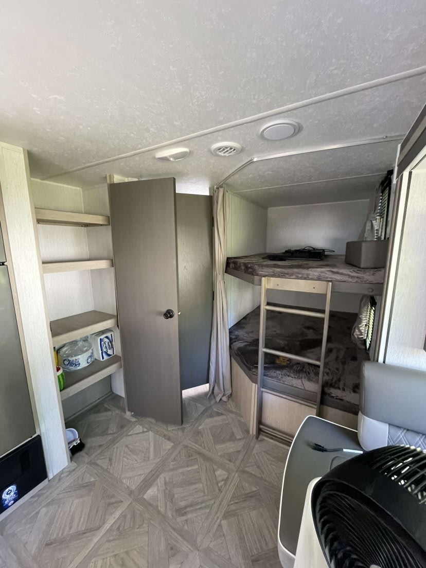 An RV rental's interior, showcasing bunk beds with a ladder, integrated storage shelves, and a distinctive patterned floor.. Forest River Wildwood X-Lite 2023