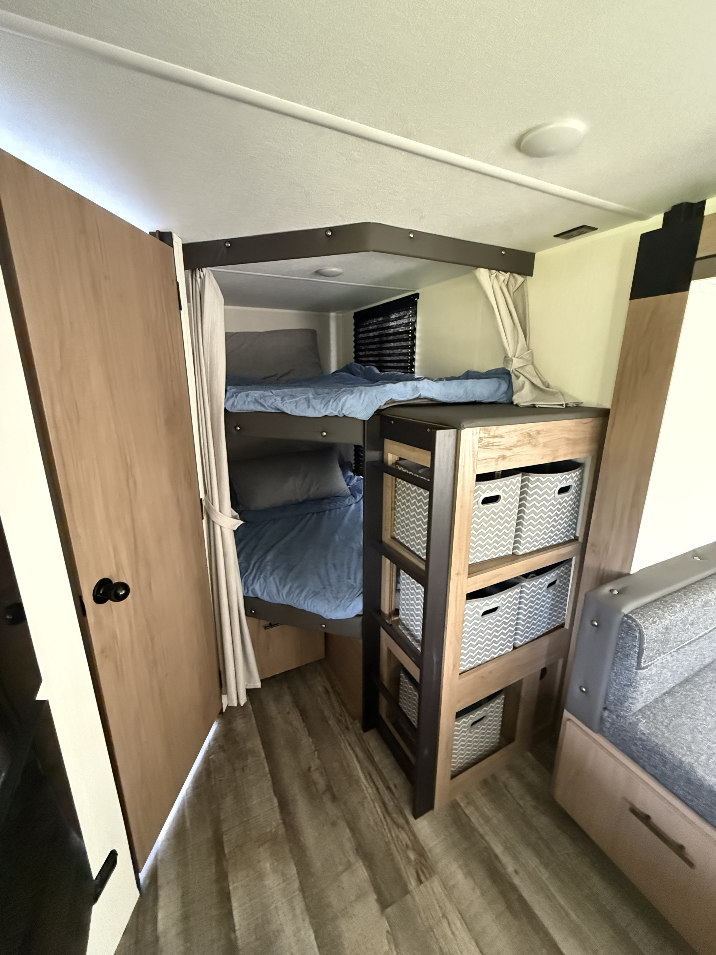 RV rental interior featuring bunk beds with blue bedding, a storage unit with patterned baskets, and wood-look flooring.. Forest River Campsite Reserve 2025