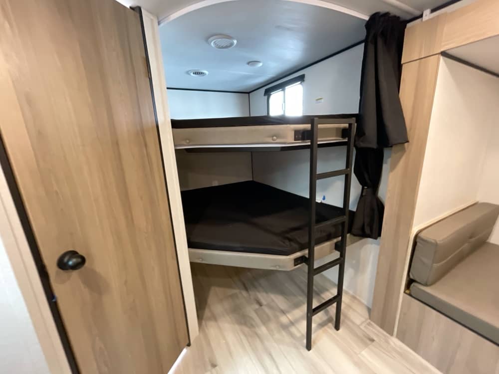 Inside this RV rental: comfortable bunk beds with black mattresses & ladder, beside a compact seating area for guests.. Keystone RV Coleman Light 2025