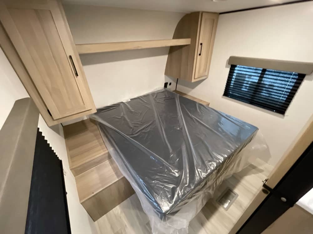 RV rental: A new, clean bedroom with a plastic-wrapped mattress, built-in wooden storage, steps, and a window.. Keystone RV Coleman Light 2025