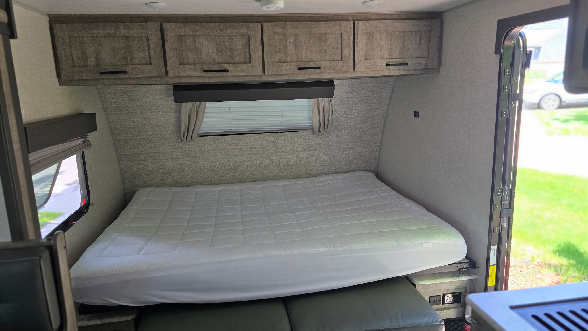 Spacious RV rental bedroom with a white mattress, overhead storage cabinets, and a window view, offering comfort on the go.. Forest River Surveyor Legend 2023