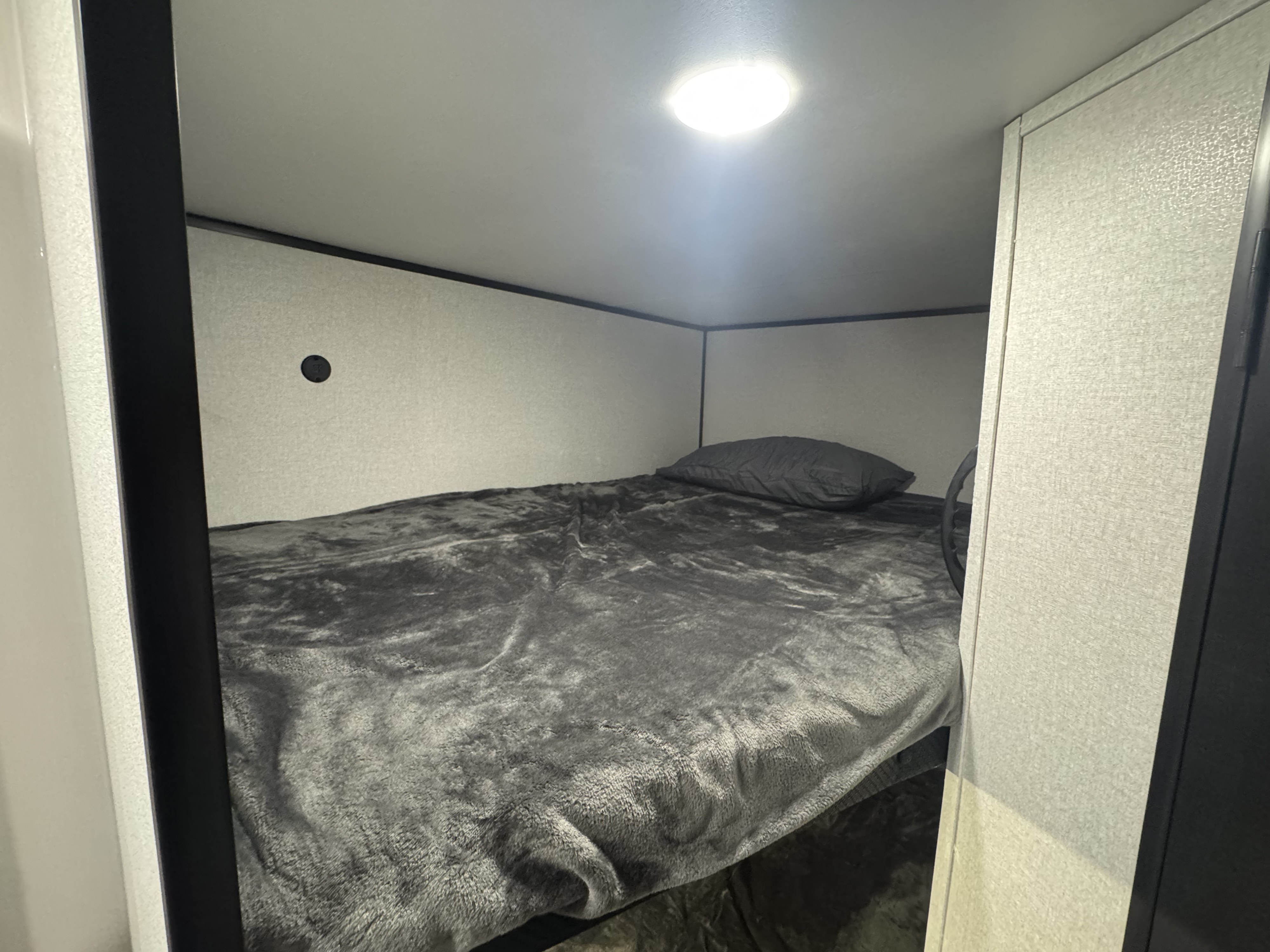 Compact RV rental bunk bed with soft grey bedding, ideal for cozy sleeping. Bright ceiling light illuminates the snug camper space.. Jayco Jay Flight SLX 197MBW Baja 2026
