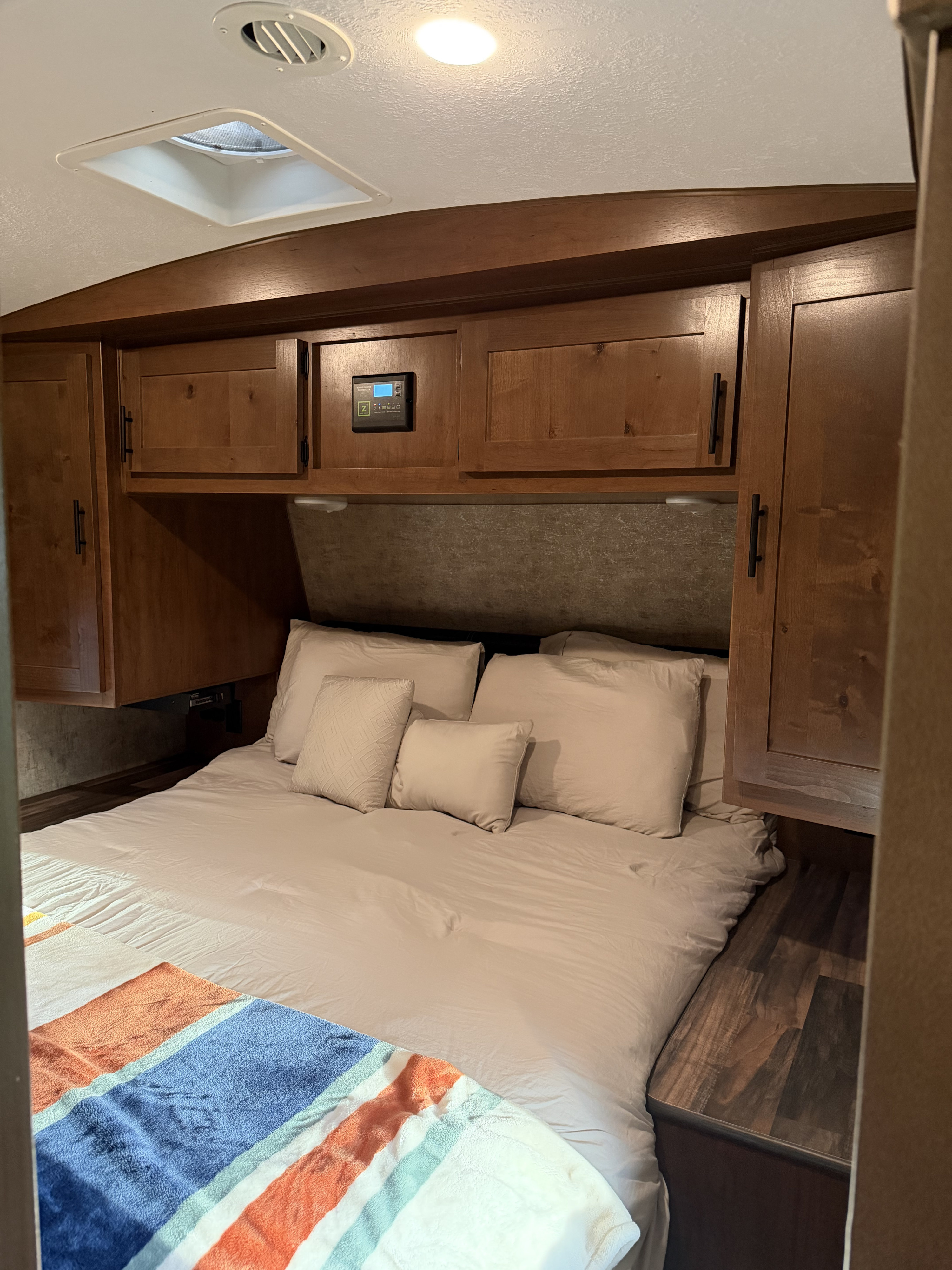 Relax in this cozy RV rental bedroom: queen bed, wood cabinets, solar controller, ceiling vent, and skylight.. Outdoors RV Mountain Trax Backcountry 2024