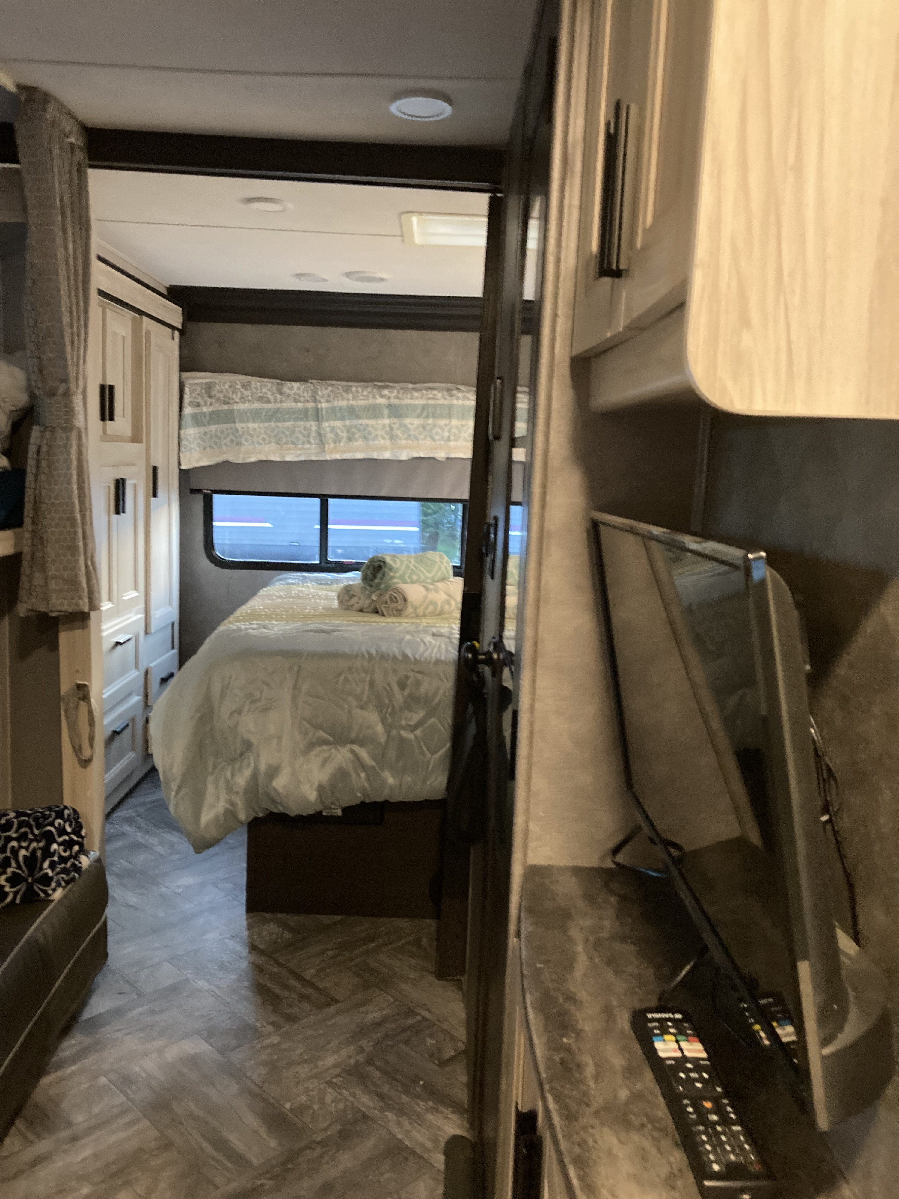 Cozy RV rental bedroom with a bed, rolled towels, window, wardrobe, TV, and chevron-patterned floor.. Forest River Sunseeker LE 2022