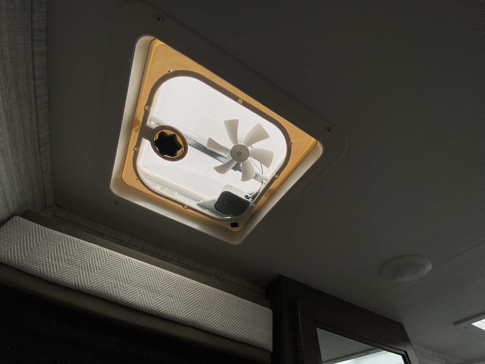 Inside an RV rental: a ceiling vent with fan and mesh screen. Below, a textured cushion is visible. Natural light enters.. Entegra Coach Odyssey SE 2025