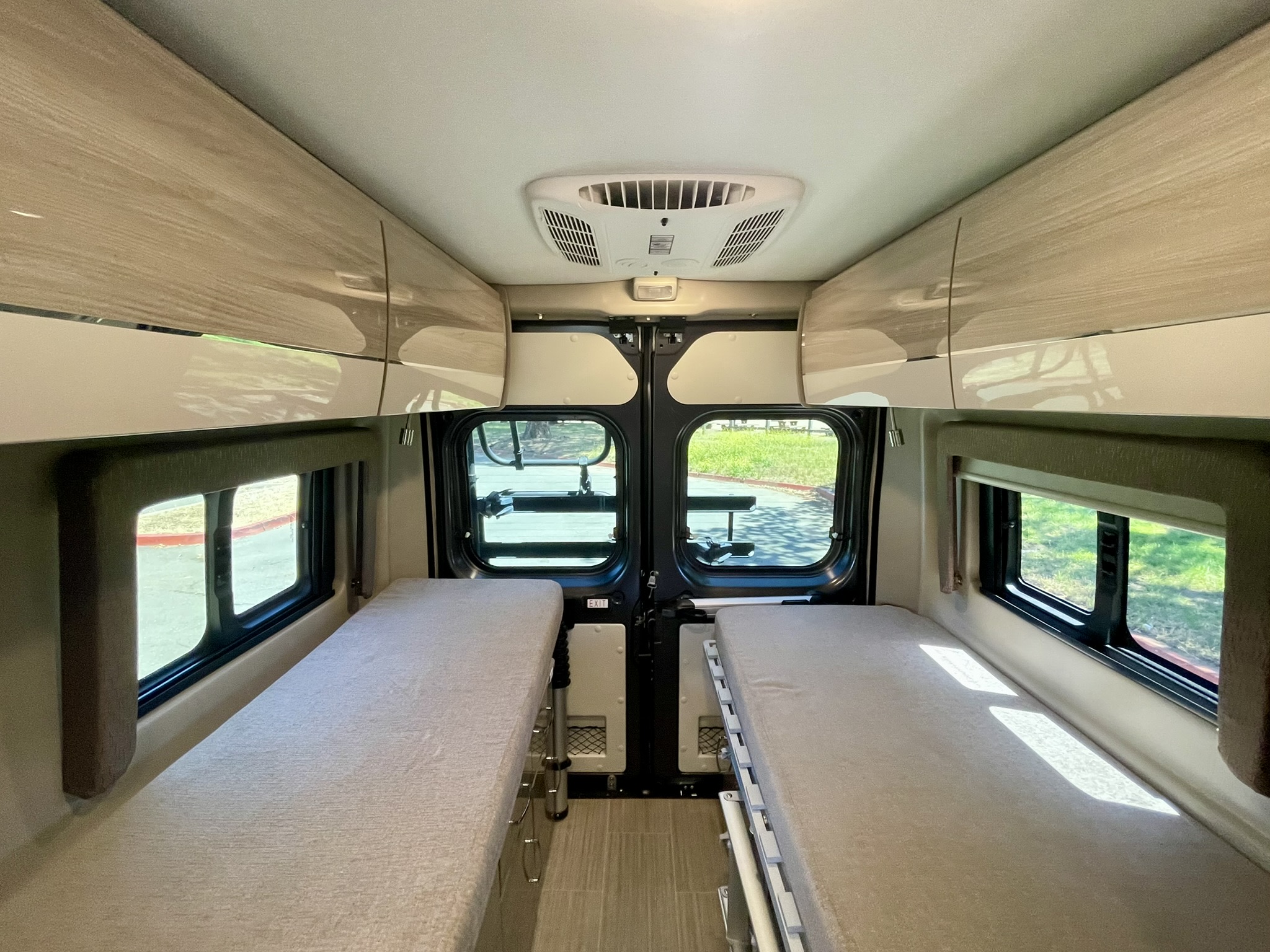 Interior view of an rv rental camper van, featuring two beds, overhead cabinets, and a ceiling AC unit for comfort.. Thor Sequence 2022