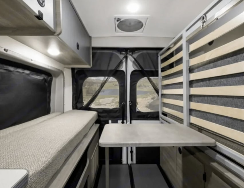 Cozy RV rental interior with a bed, movable table, and storage. Enjoy scenic views from this compact camper van.. Winnebago Solis 2021