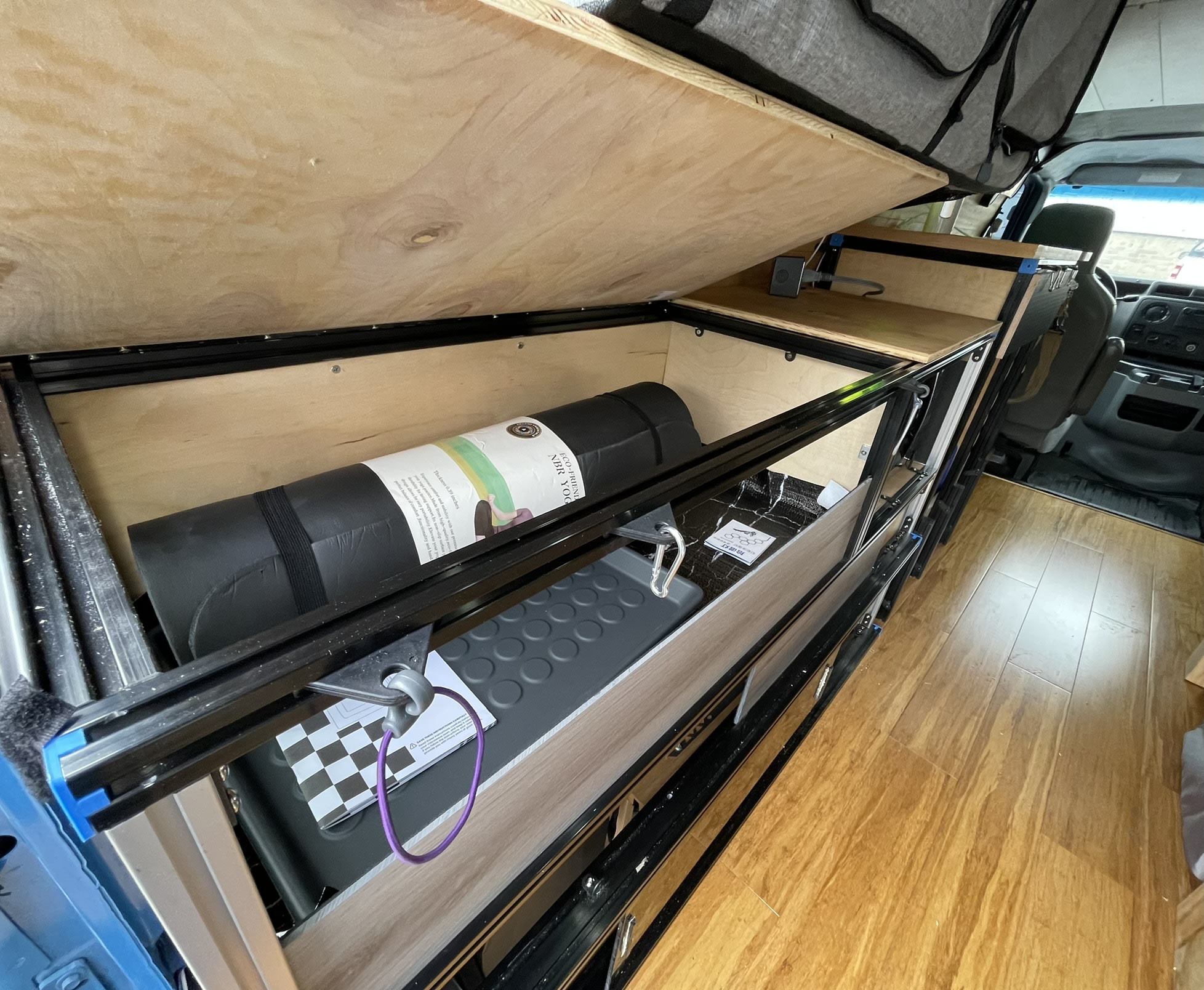 RV rental's clever interior: bed platform lifted, showing yoga mat storage & pull-out kitchen unit, bamboo floor, driver's cabin visible.. Ford E350 2010