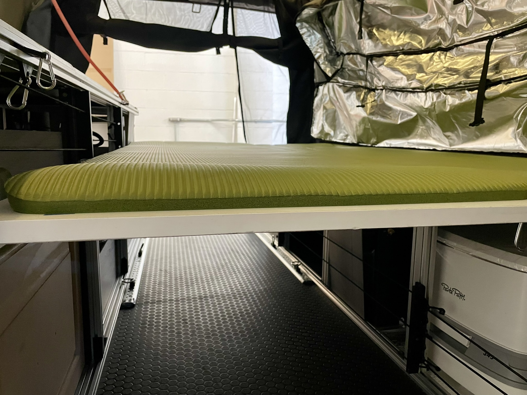 Compact RV rental interior featuring a comfortable sleeping pad, under-bed storage, and a portable Porta Potti for adventure travel.. Chevy Express 1500 1998