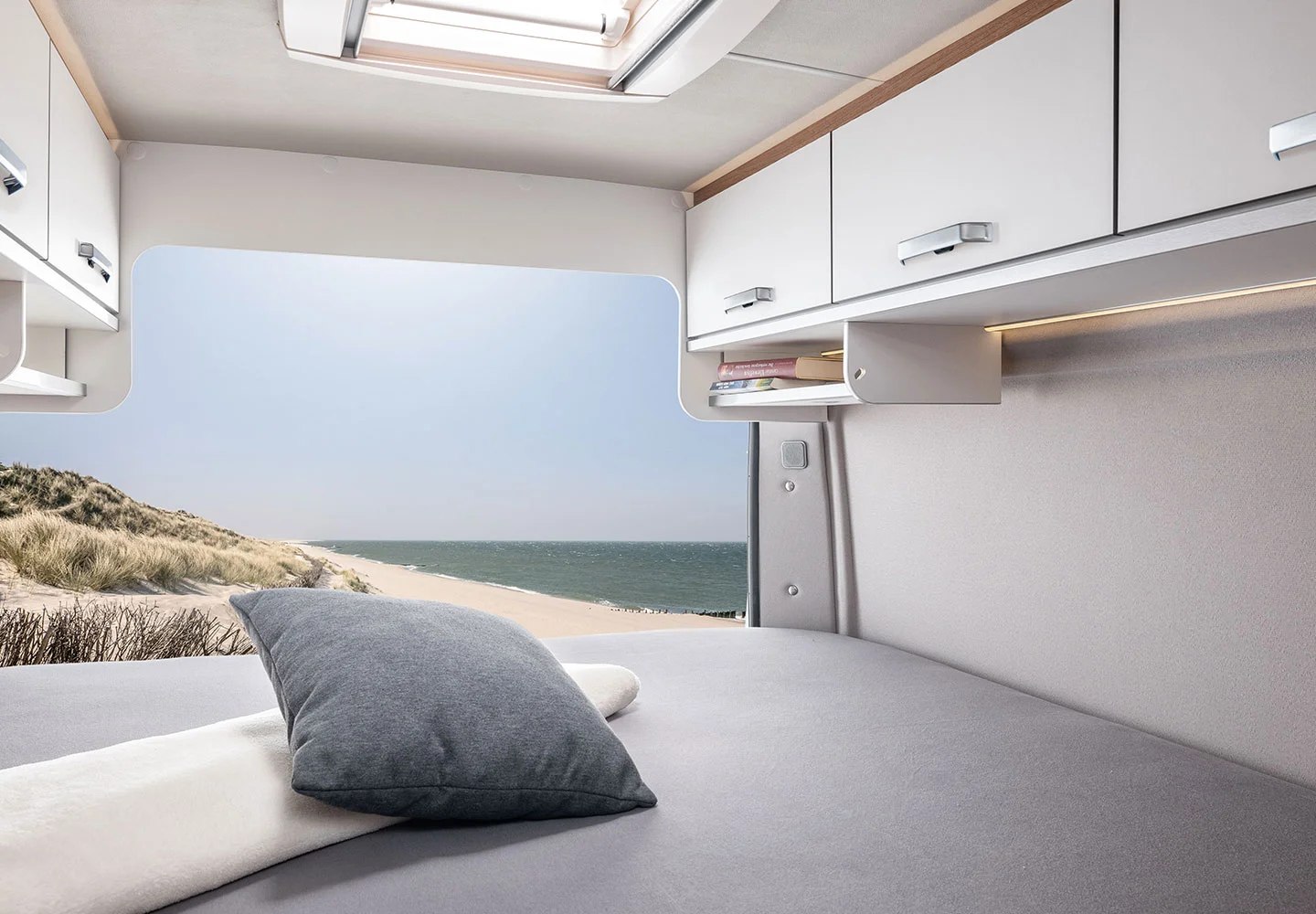 RV rental: Enjoy a cozy bed with an ocean beach view from this modern interior, featuring overhead storage, a reading nook, and a skylight.. Fiat Ducato 2026