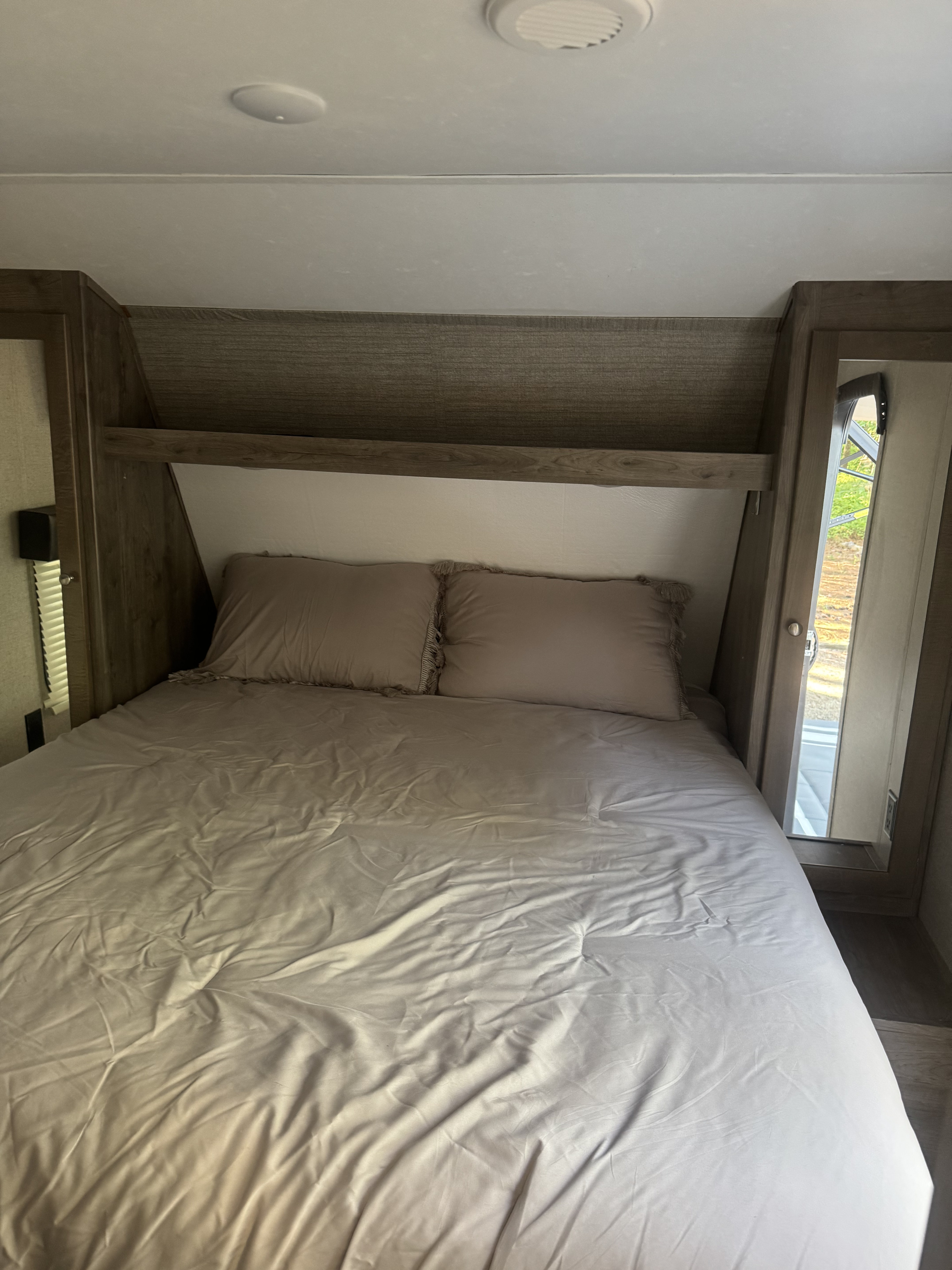 This RV rental bedroom features a comfy bed with pillows, overhead storage, and an open side window revealing a view of nature.. Aspen Trail Aspen Trail Trailer 2018