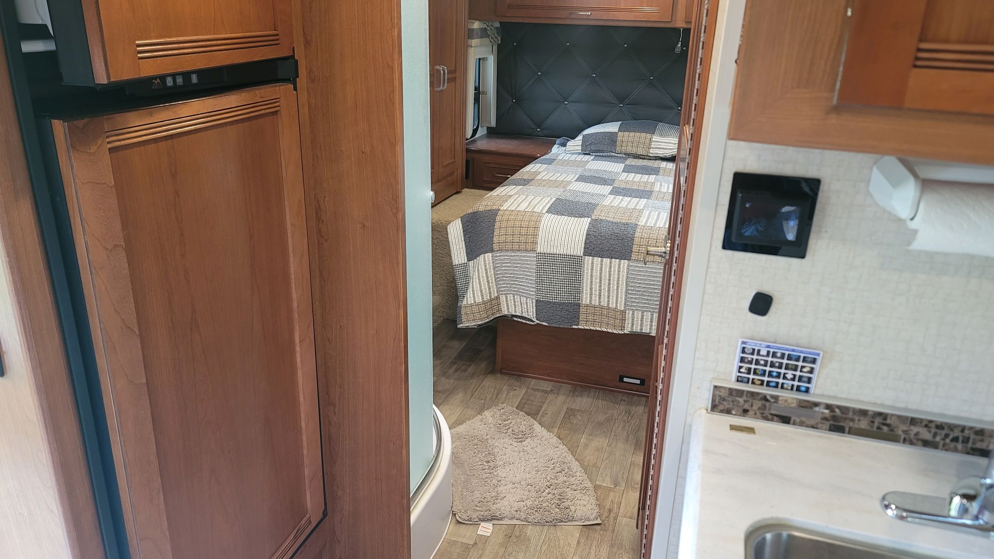 Inside an RV rental: a bedroom with a quilted bedspread, small kitchen area with sink, and built-in fridge.. Winnebago Aspect 2018