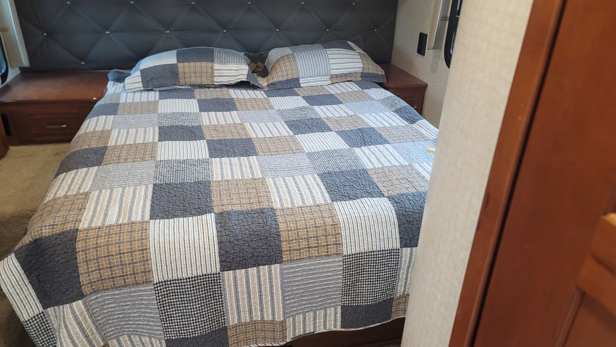 RV rental bedroom: patchwork quilted bed in gray, white, and tan, with a dark tufted headboard & wood nightstands.. Winnebago Aspect 2018