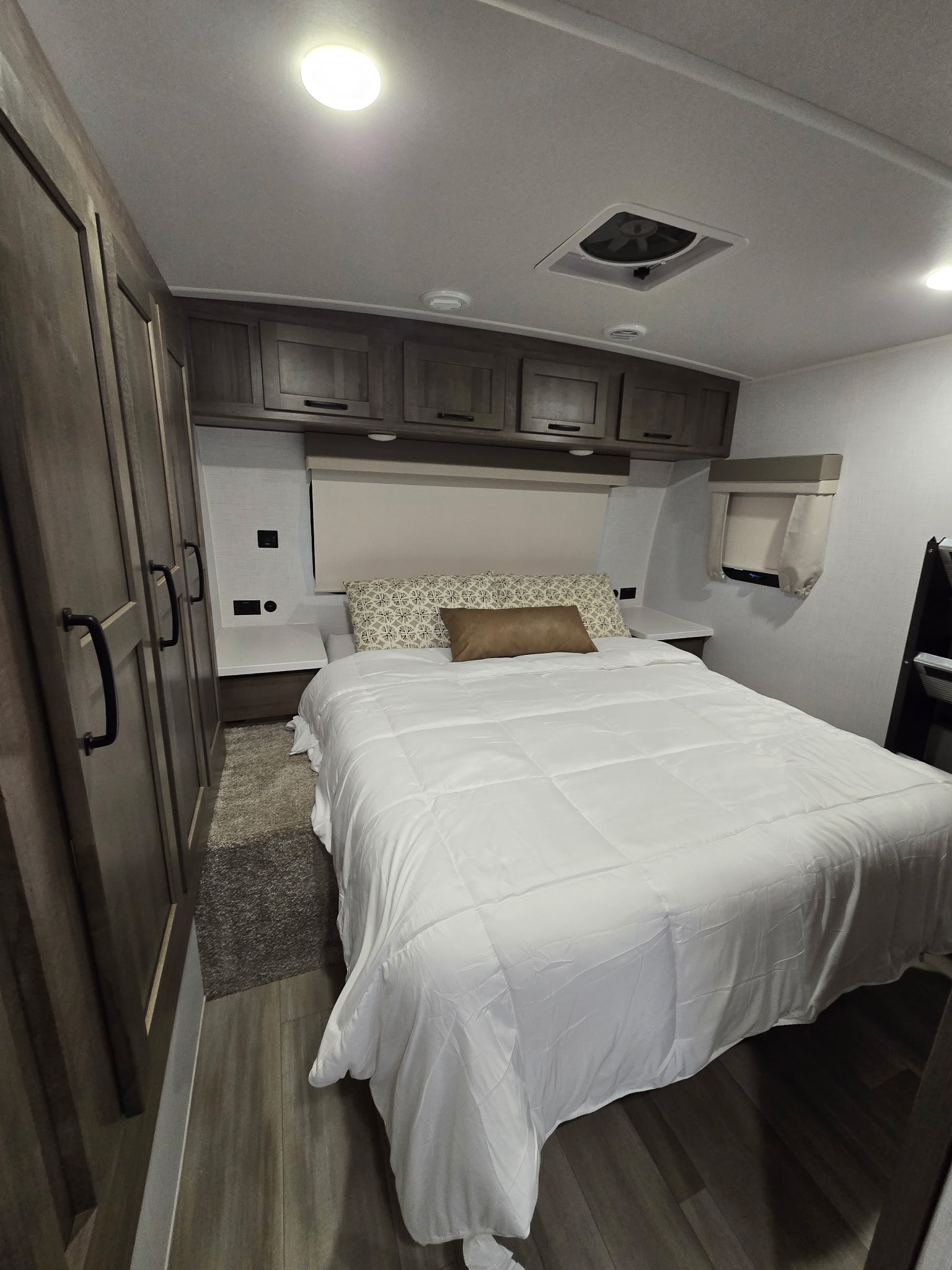 RV rental bedroom with a comfortable queen bed, overhead cabinets, vent fan, and wood flooring.. Forest River Flagstaff Super Lite 2024