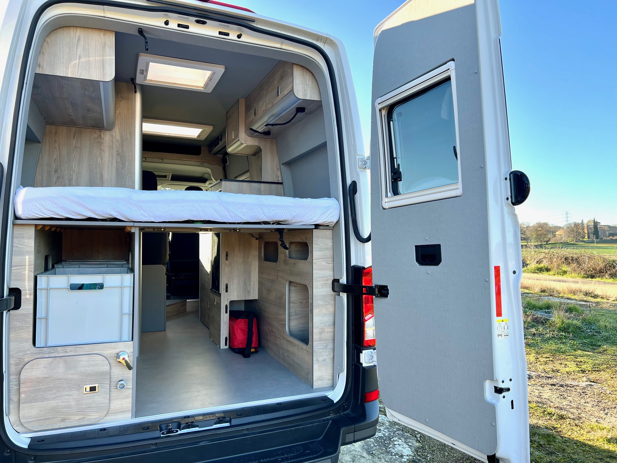Spacious RV rental camper van interior with bed, storage, and open back doors. Perfect for travel adventures!. Volkswagen Crafter 2025