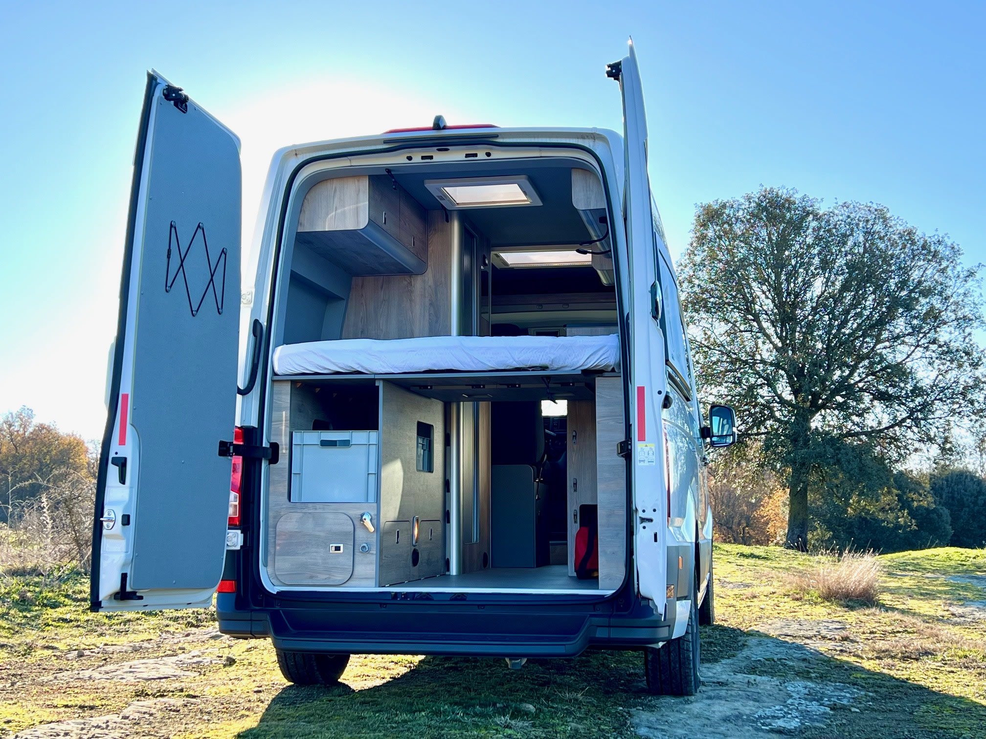 Open back of an RV rental showing its well-designed camper interior with a bed, storage, and natural light, ready for travel.. Volkswagen Crafter 2025