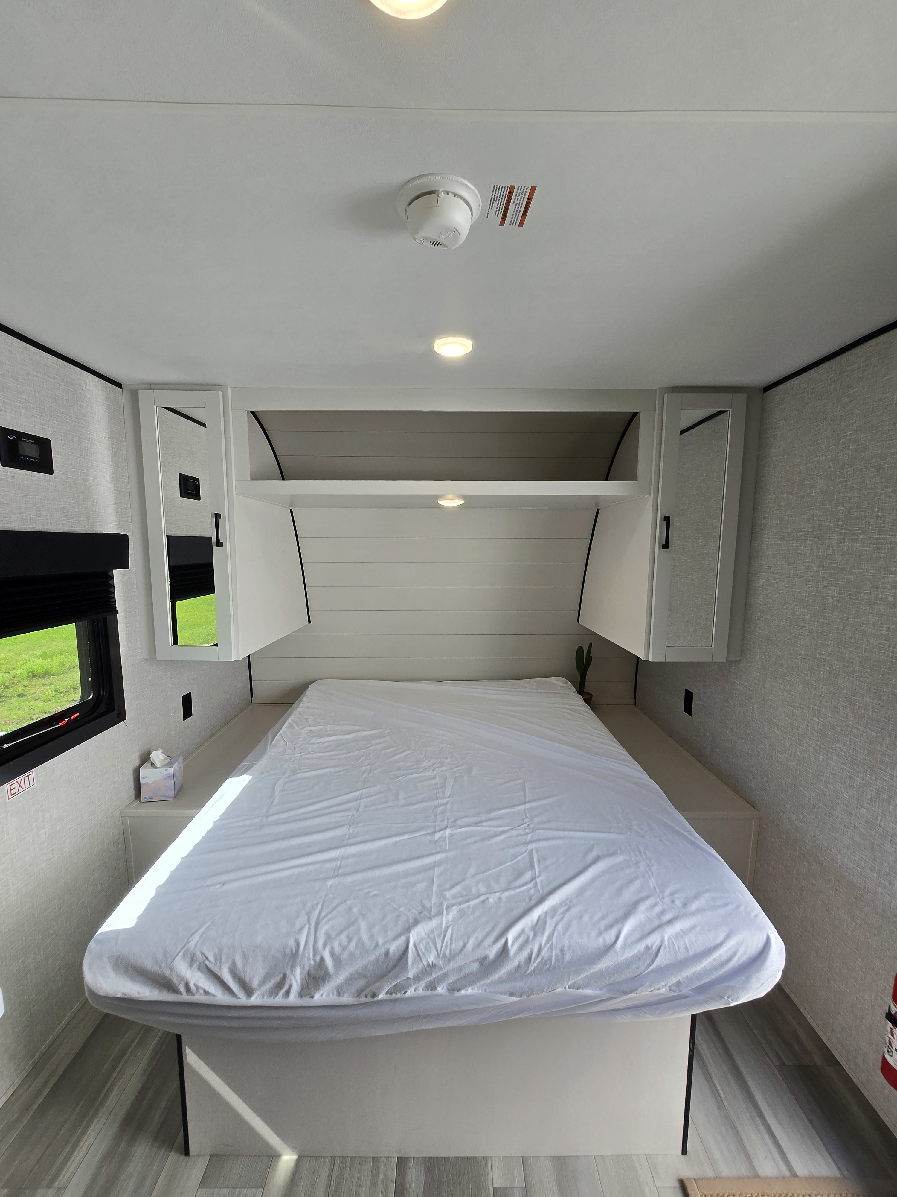 This bright RV rental bedroom features a comfy bed, overhead cabinets, and a window view, offering a modern, compact sleeping area.. Starcraft Autum Ridge 2025