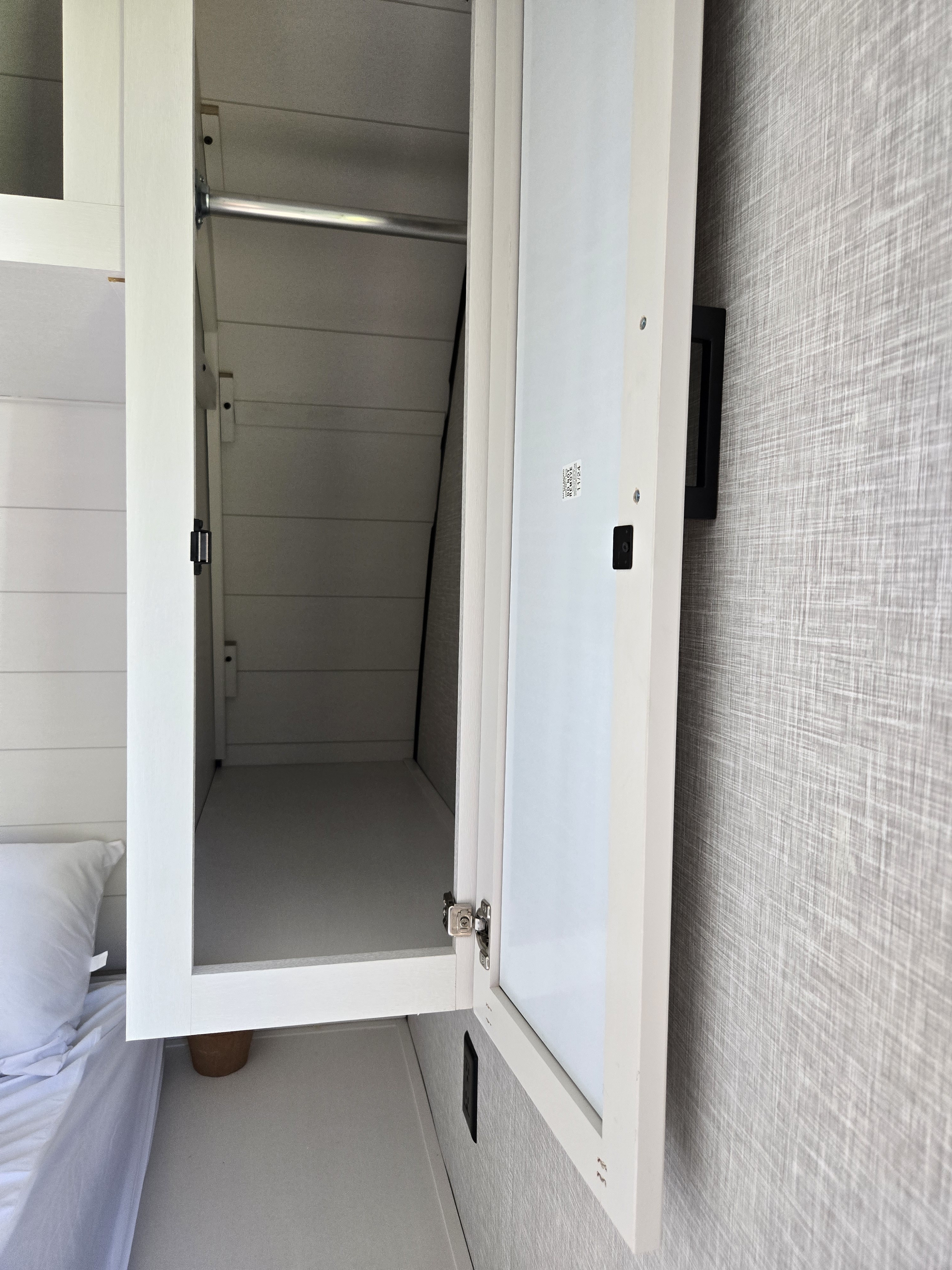RV rental: An open white closet door revealing an empty closet with a hanging rod, next to a bed and textured wall.. Starcraft Autum Ridge 2025