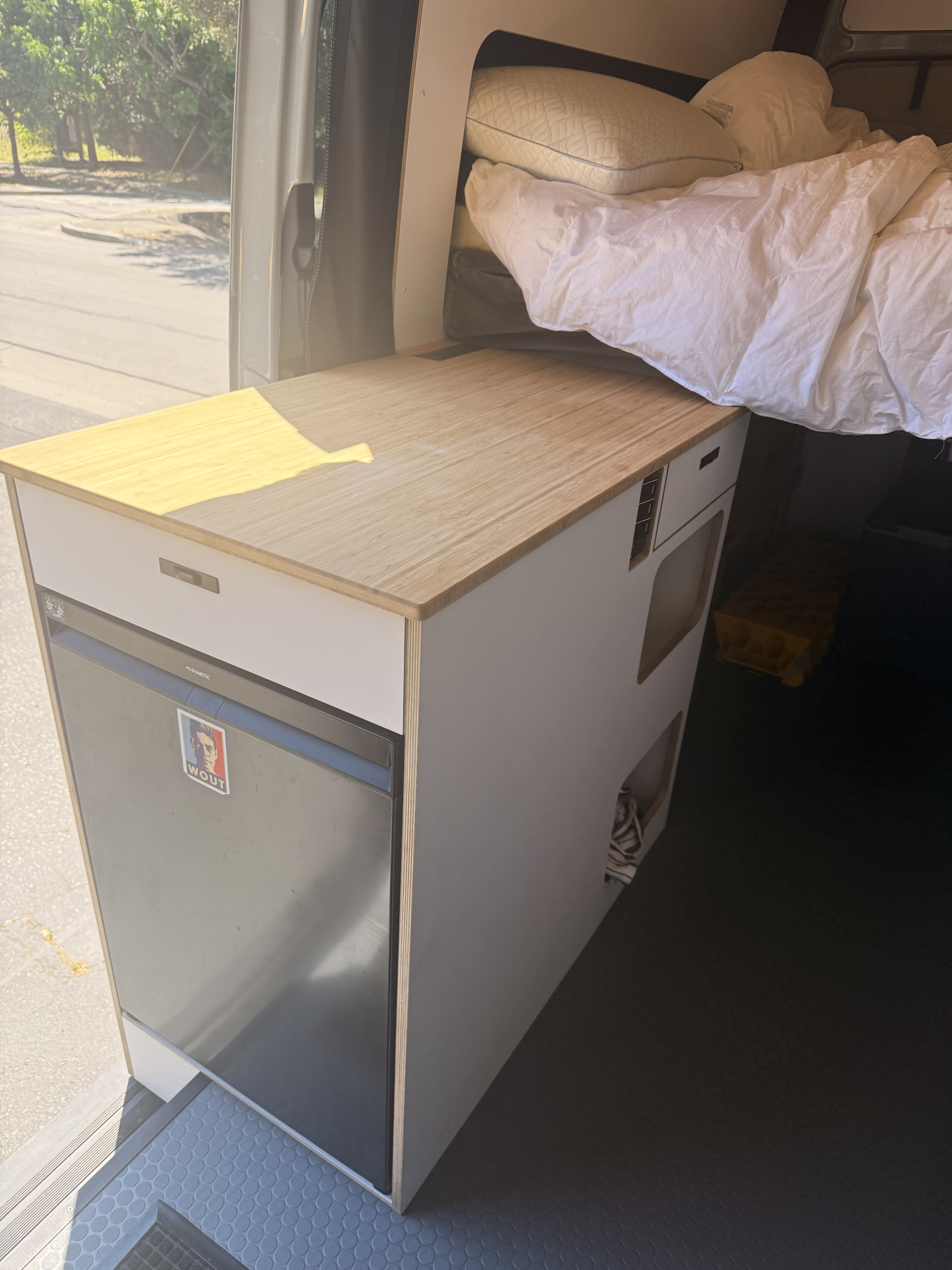 Cozy RV rental campervan interior with a compact kitchen, Dometic fridge, wooden counter, and a comfortable bed.. Mercedes Sprinter 2026