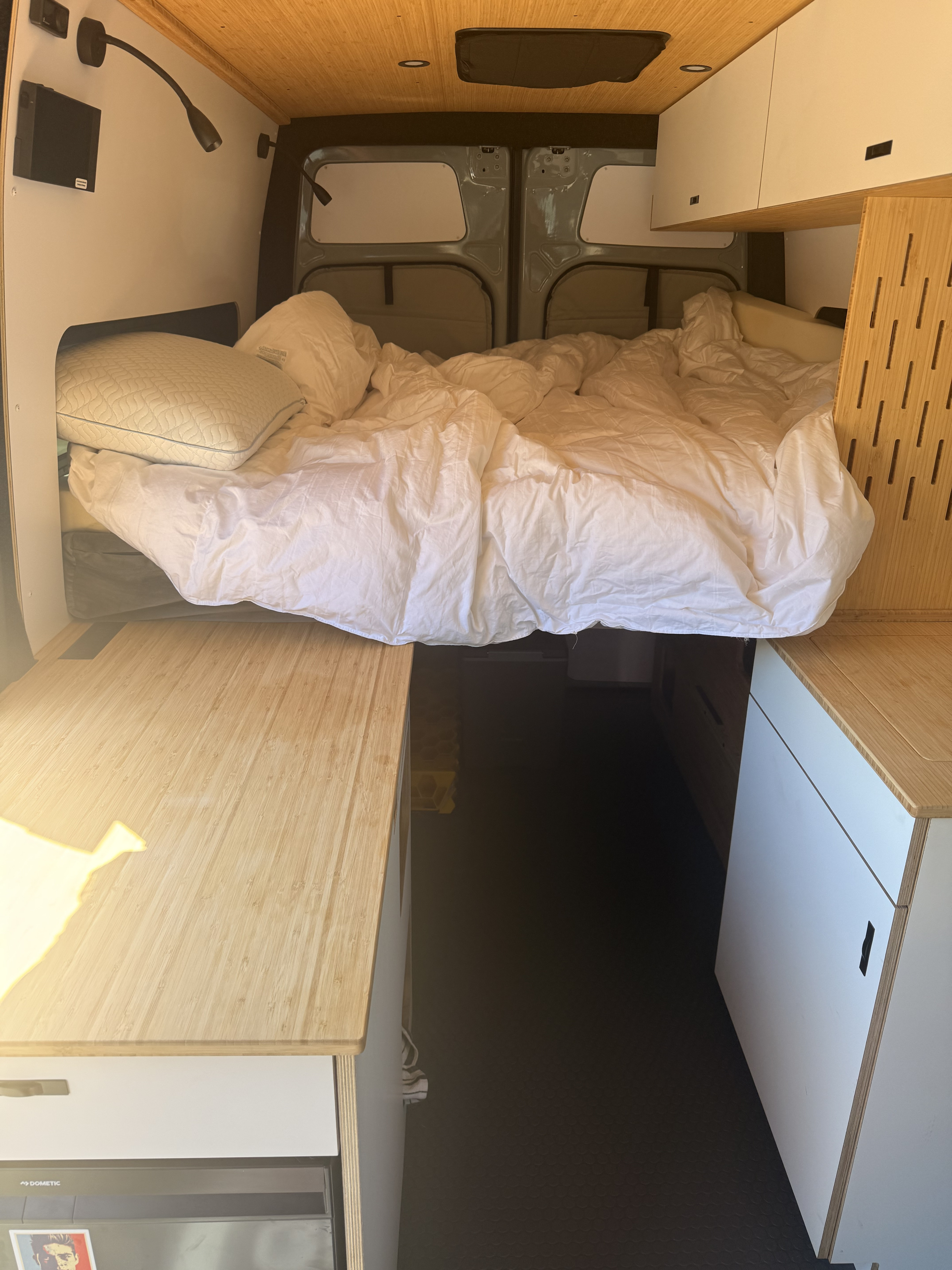 Inside a modern RV rental camper van: comfortable bed, bamboo counters, storage, and Dometic fridge for adventures.. Mercedes Sprinter 2026