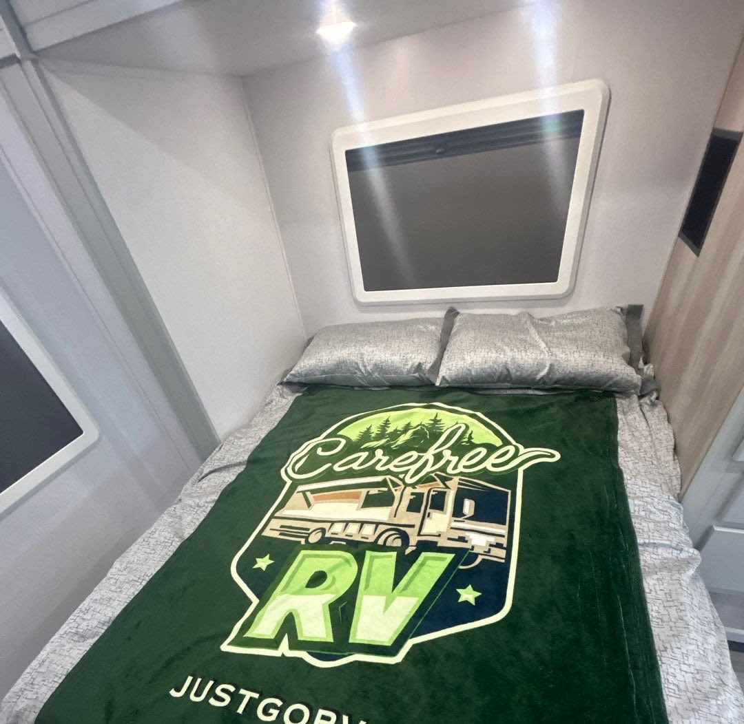 Cozy rv rental bedroom showing a bed with a green "Carefree RV" blanket and two pillows. Ideal for your next trip.. Isata 3 Series 2026
