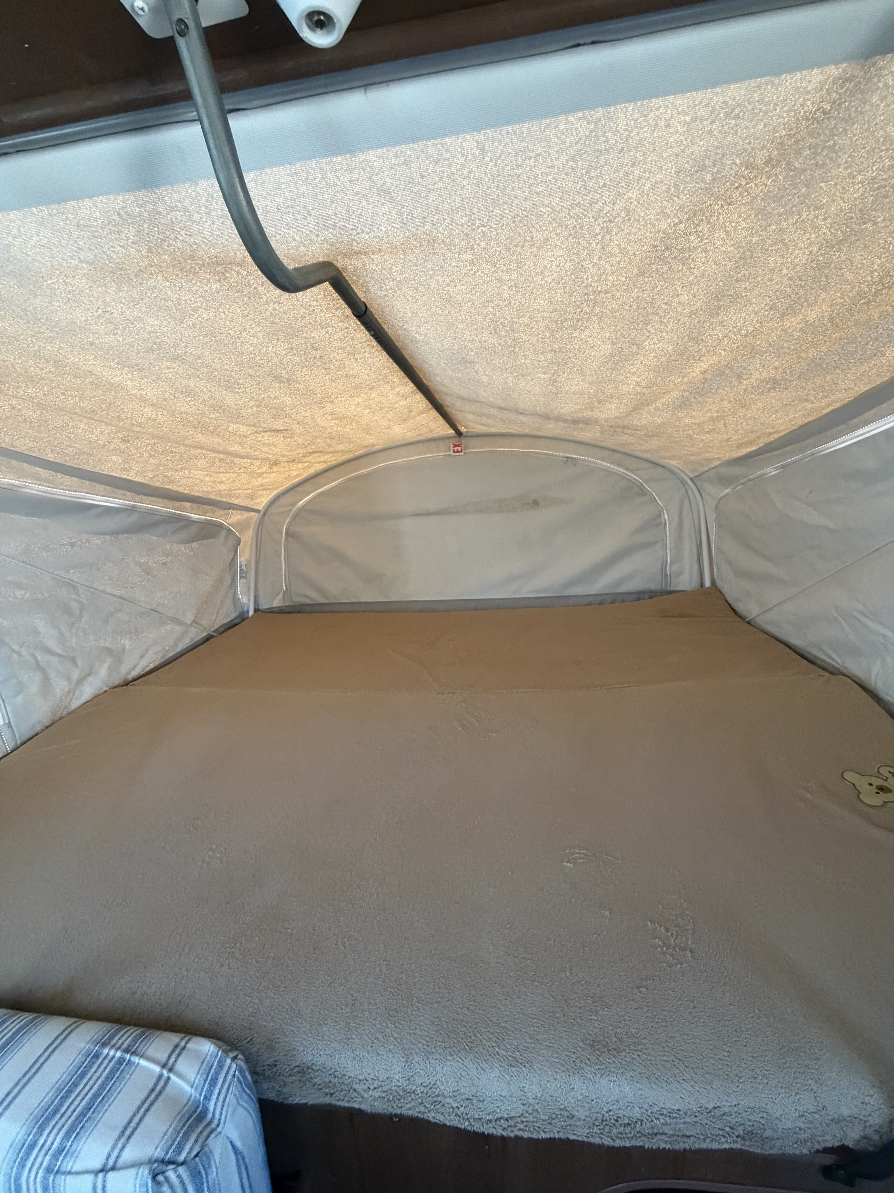 Cozy bed inside an rv rental pop-up camper, featuring fabric walls/ceiling and a soft blanket with a teddy bear.. Jayco Jay Feather 2017