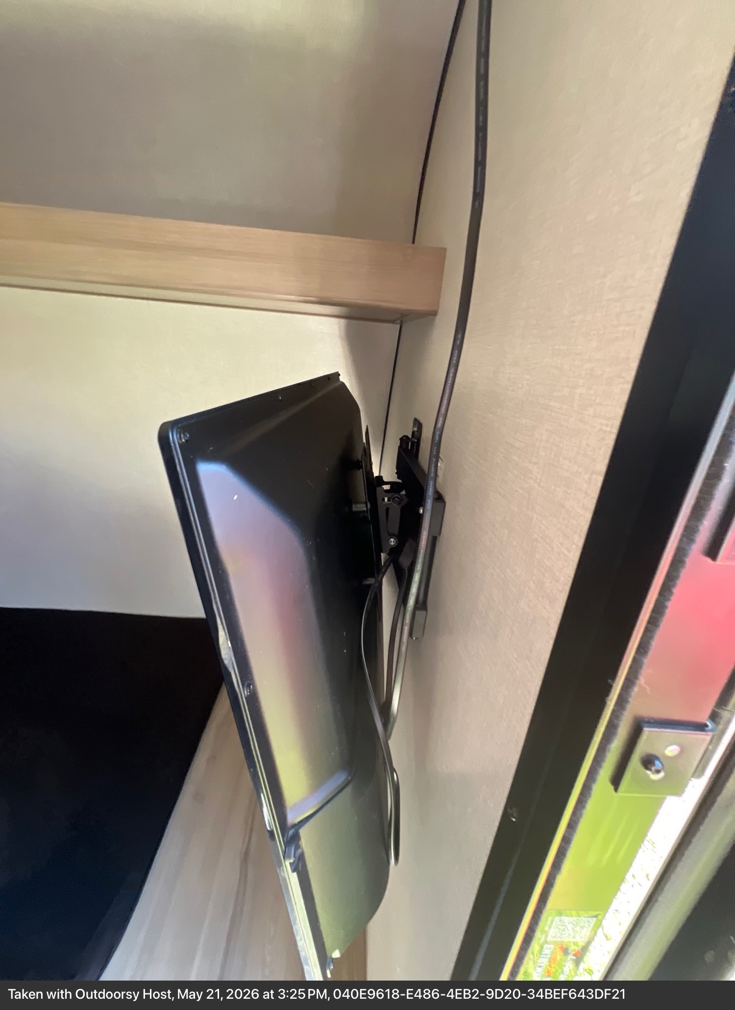 Wall-mounted TV inside an RV rental, angled to the side with visible cables and a light wood shelf above for onboard entertainment.. Keystone RV Coleman 13B 2026