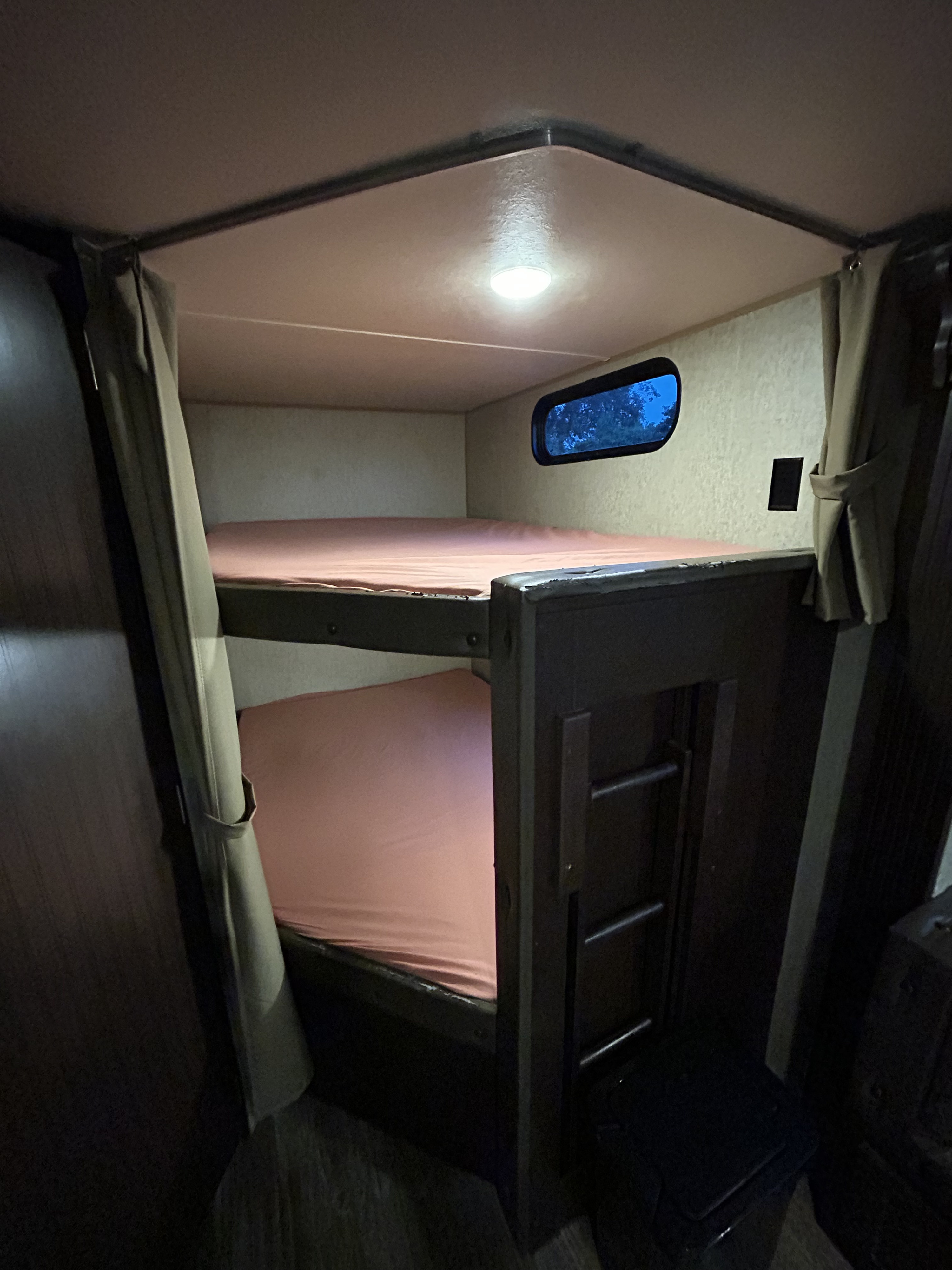 Cozy RV rental bunk beds with pink sheets, an overhead light, and a small window showing evening sky. Ideal for compact sleeping.. Forest River Cherokee 2016