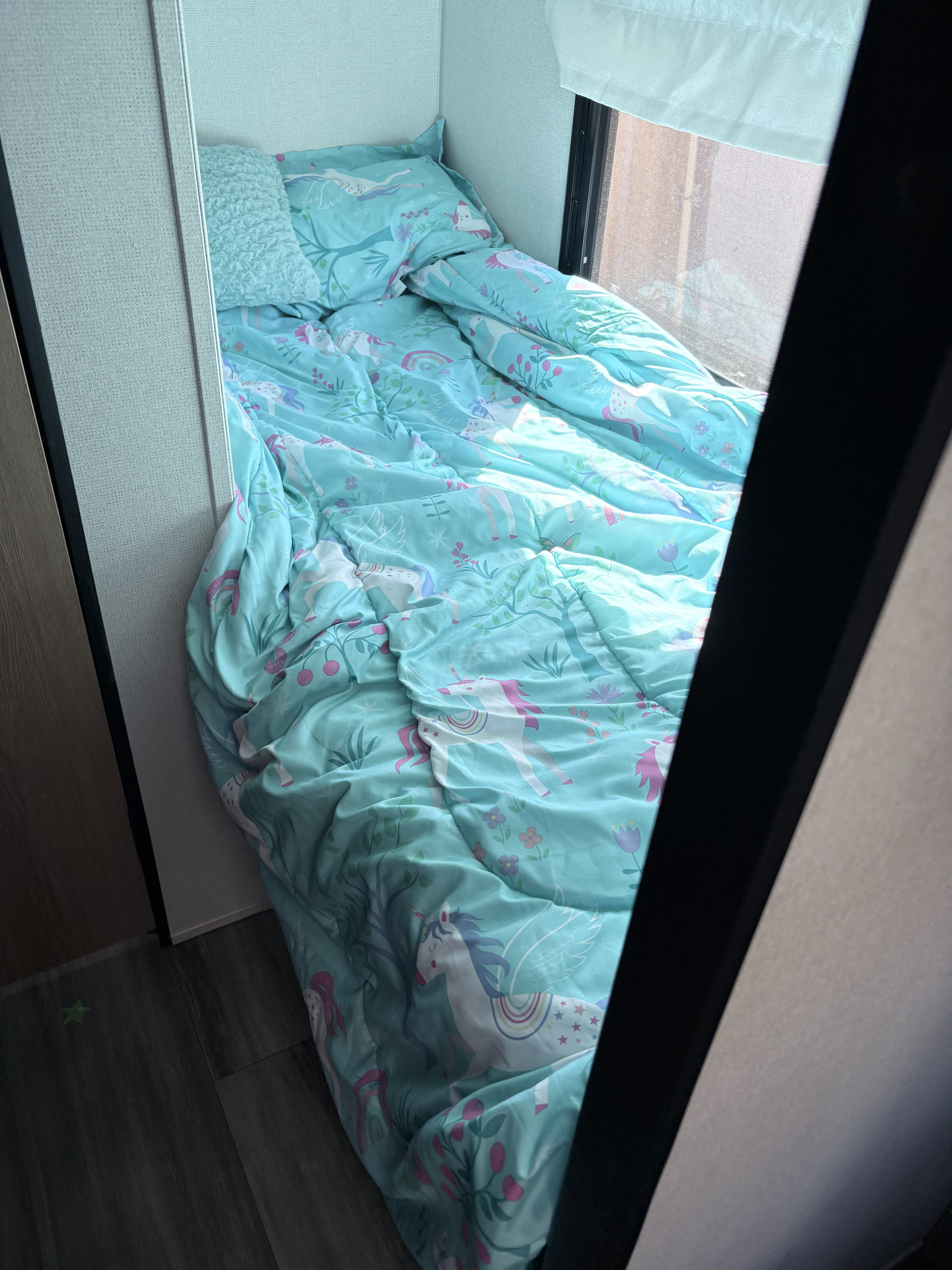 RV rental bunk bed featuring whimsical light blue unicorn bedding, a fluffy pillow, and dark wood flooring.. Forrest River Primetime Avenger 2024