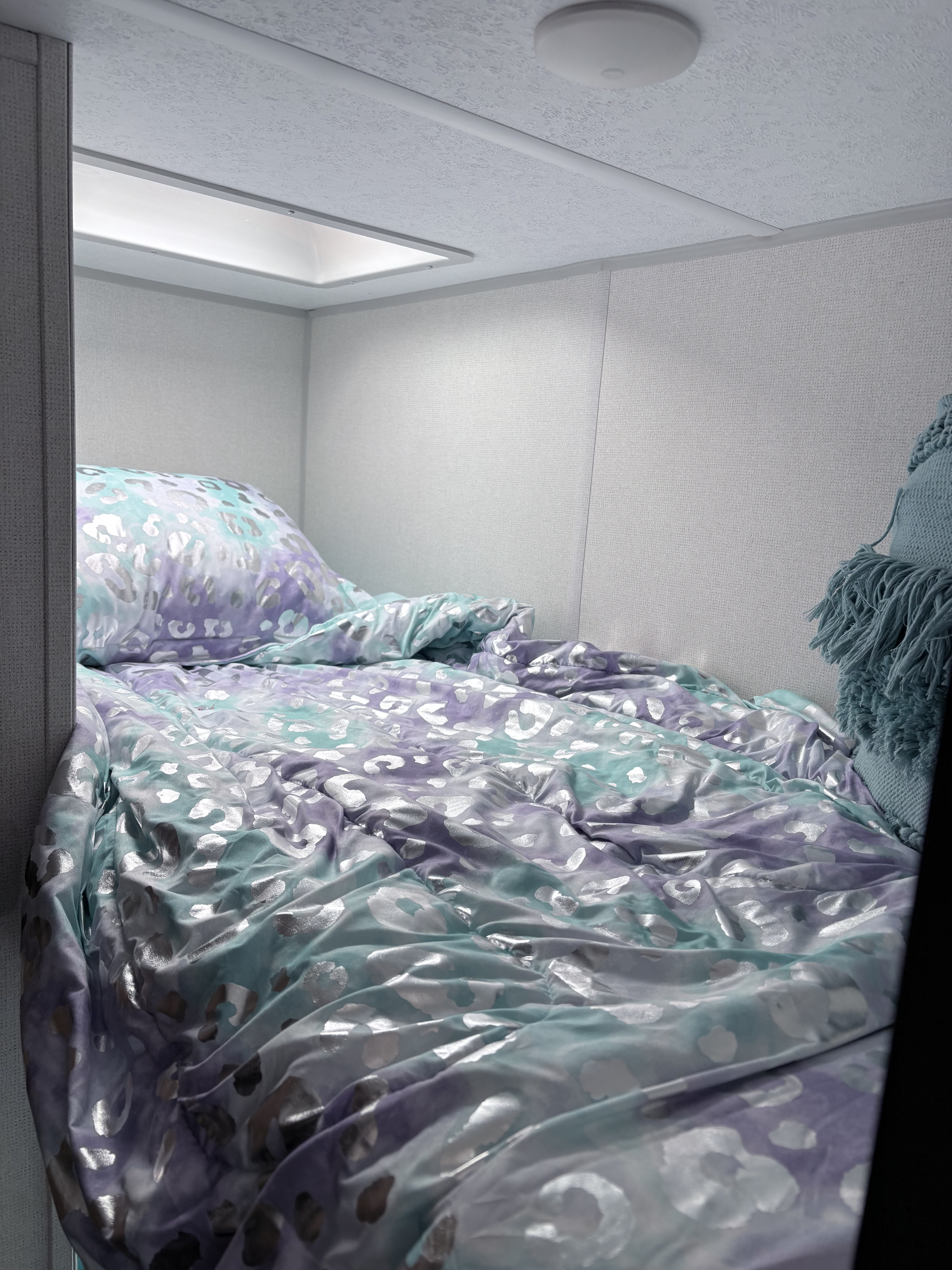 Cozy RV rental sleeping area with a vibrant purple & teal leopard print comforter and pillow. Compact bedroom space.. Forrest River Primetime Avenger 2024