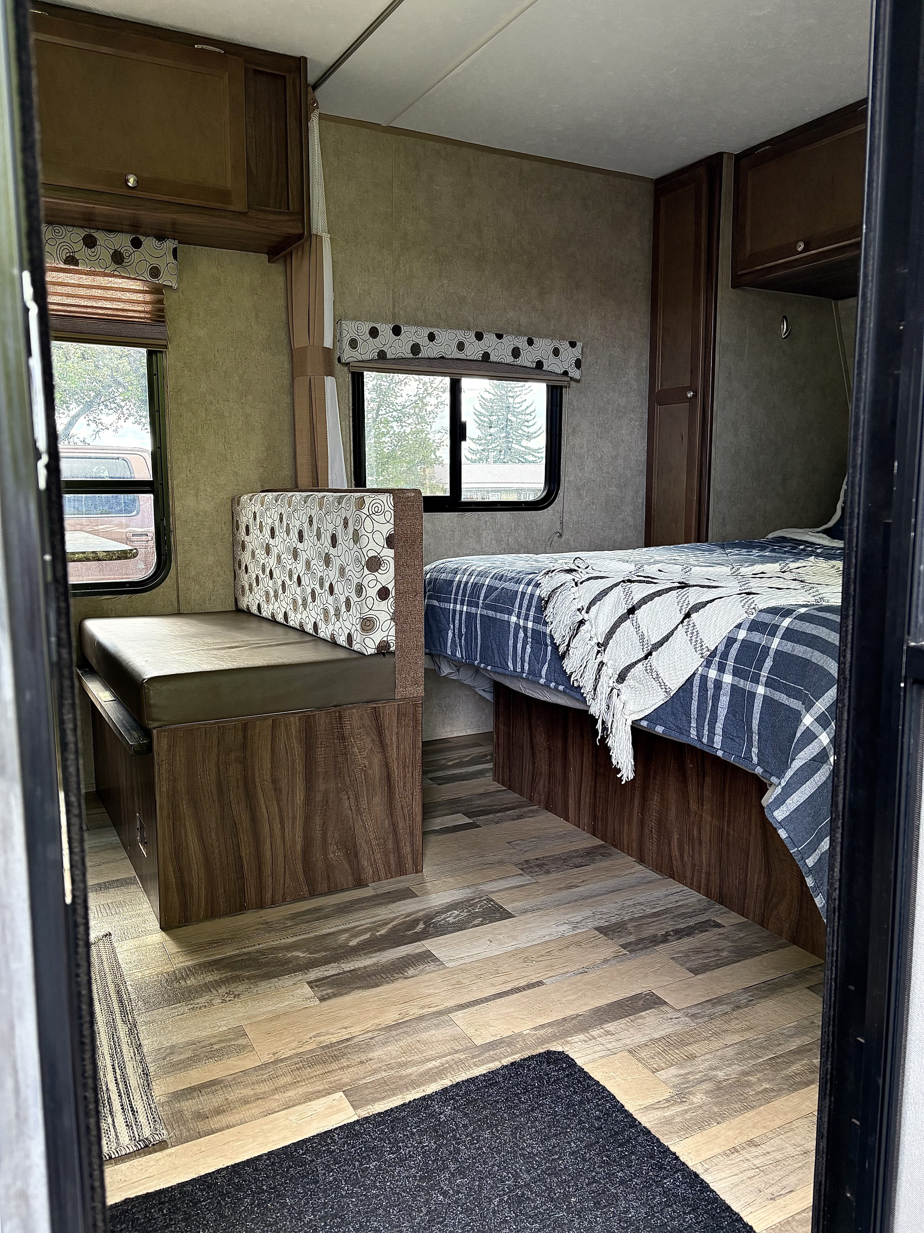 Cozy rv rental interior showing a bed with plaid bedding, dinette, windows, and wood-look flooring.. Coachmen Clipper 2017