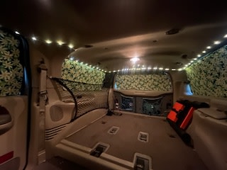 Inside this converted vehicle, ideal for an RV rental, discover custom leaf-pattern curtains, ambient LED lights, and a ready-to-sleep rear cargo area.. Ford Excursion 2000