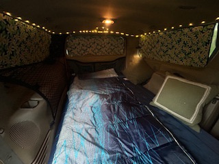 This cozy RV rental's van interior features a comfortable bed, string lights, & patterned window coverings for travel.. Ford Excursion 2000