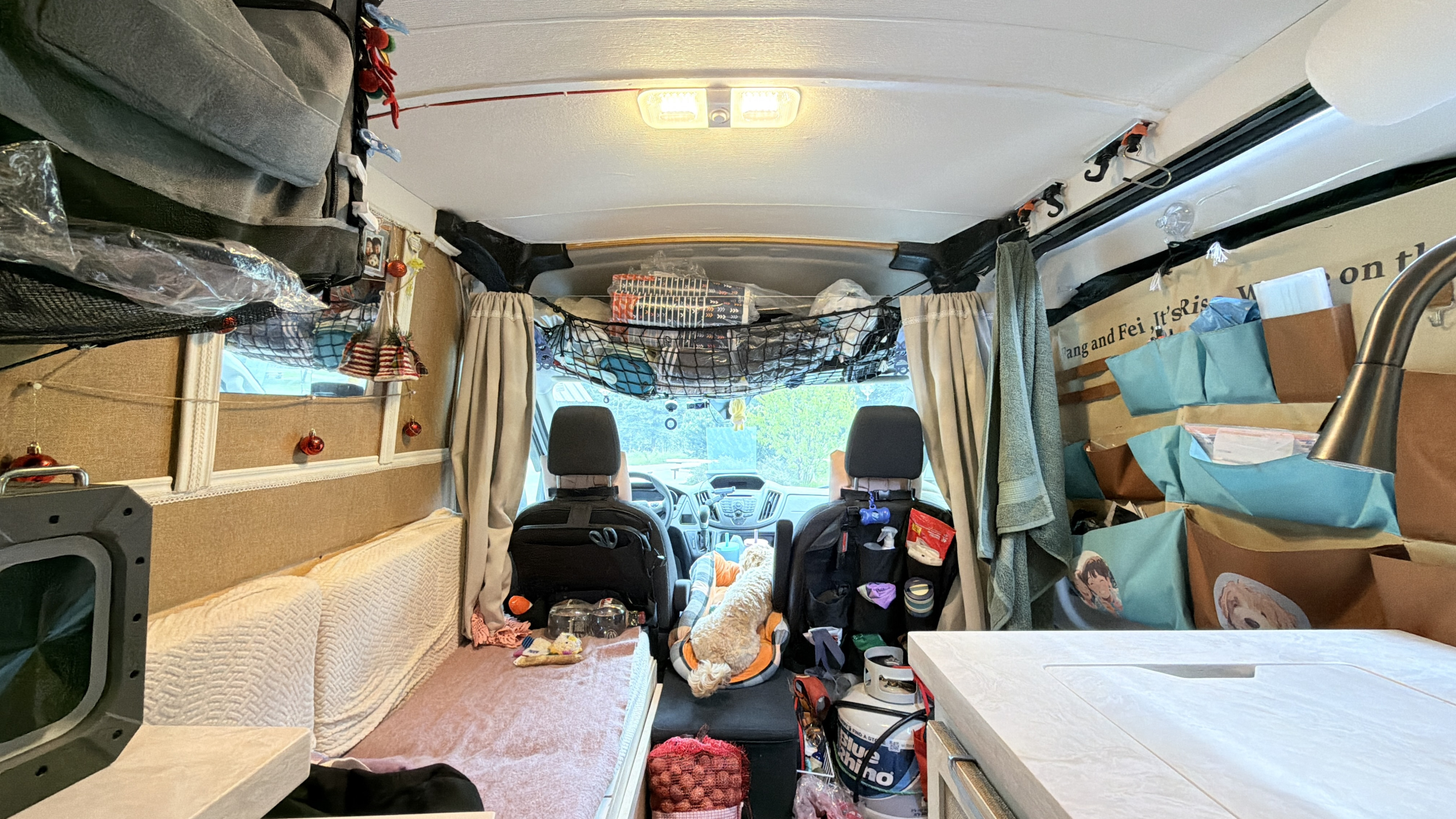 Cozy RV rental interior: Organized camper van with sleeping area, kitchen, driver's seats, pet bed, and clever storage solutions.. Ford Transit custom 2018