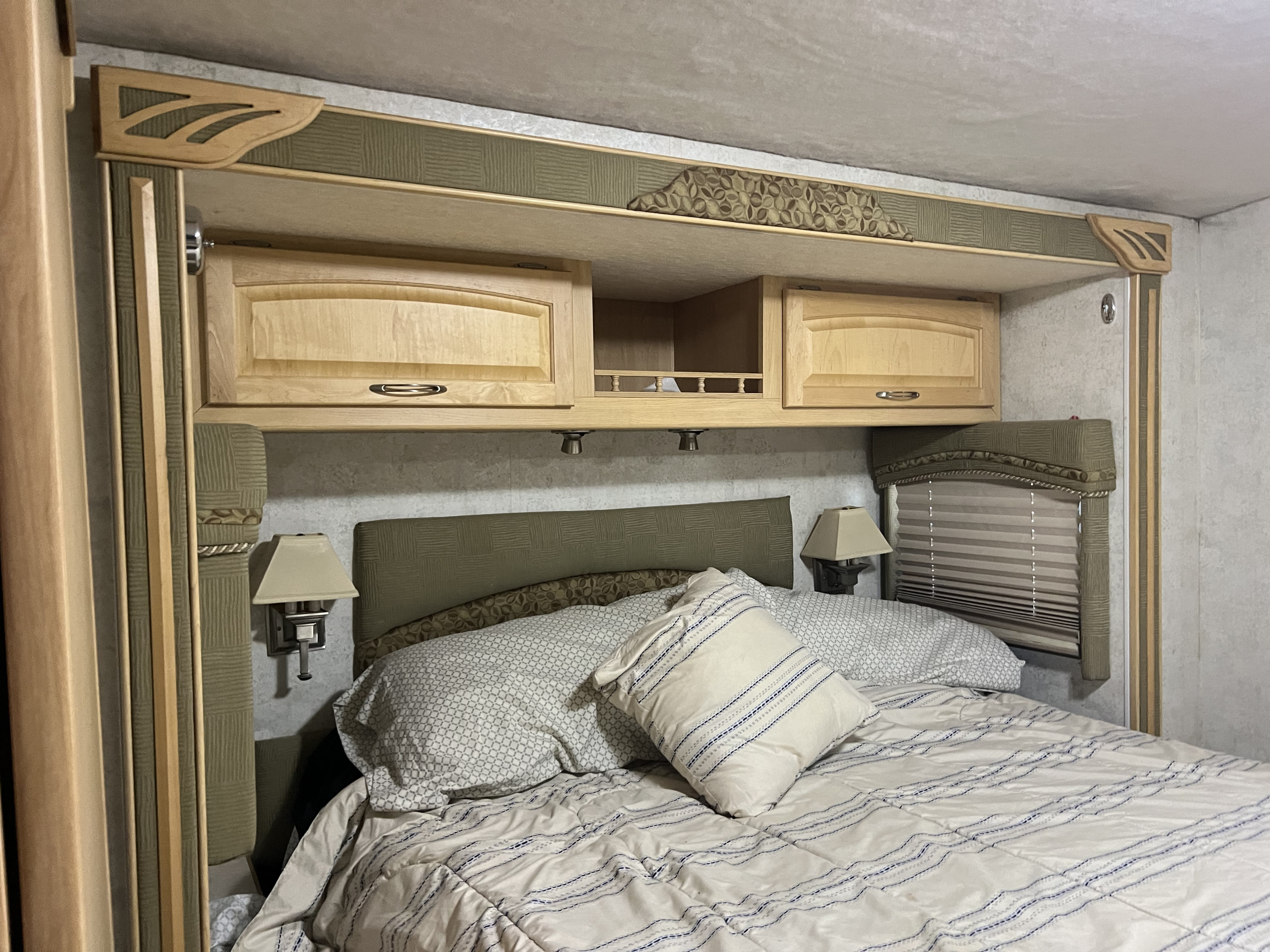 Comfortable RV rental bedroom featuring a bed with patterned bedding, upholstered headboard, and wooden overhead storage cabinets.. Winnebago Ifg33v 2005