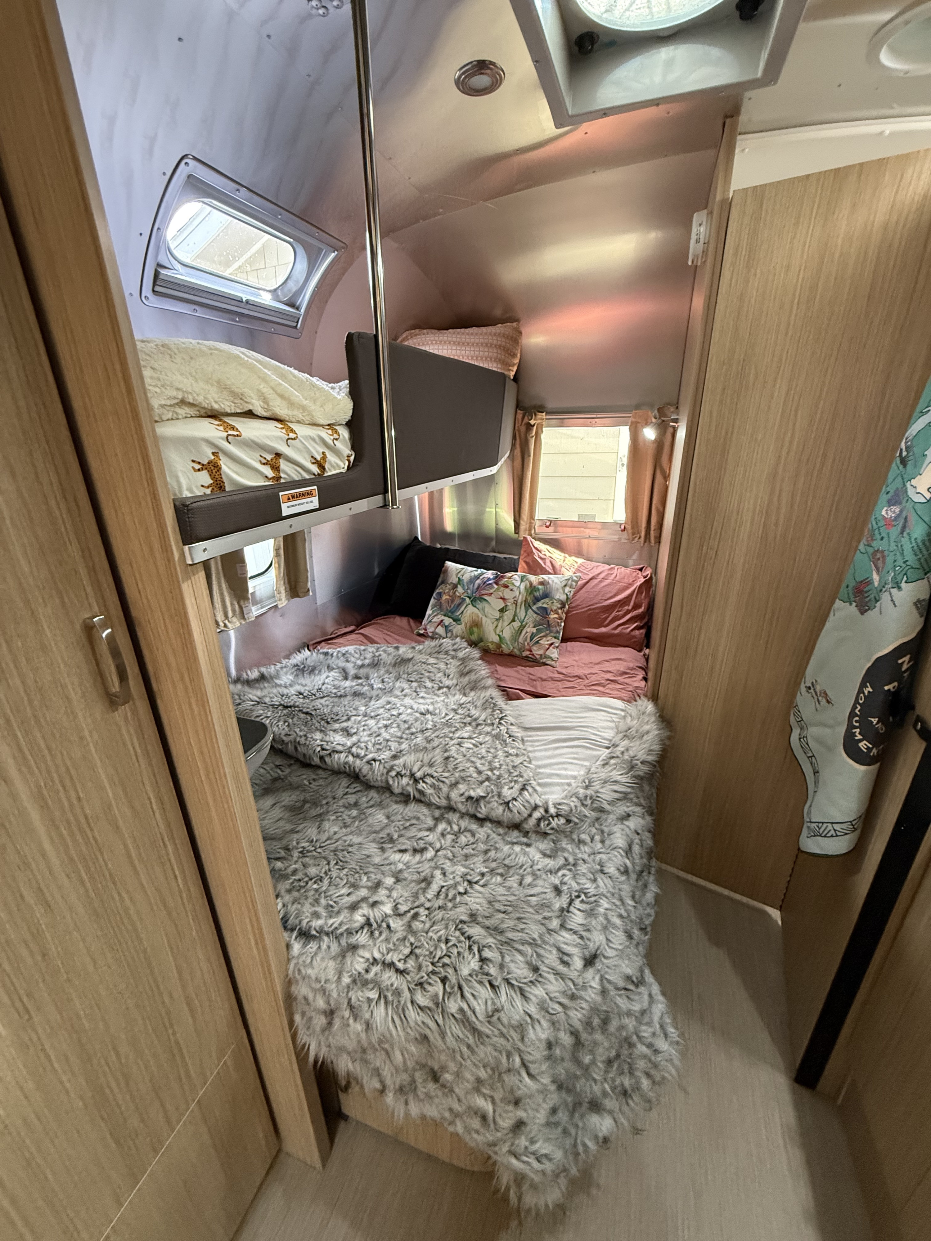 Cozy RV rental sleeping area. Features a main bed with fluffy throw, plus bunk beds with cheetah-print sheets.. Airstream Flying Cloud 2018