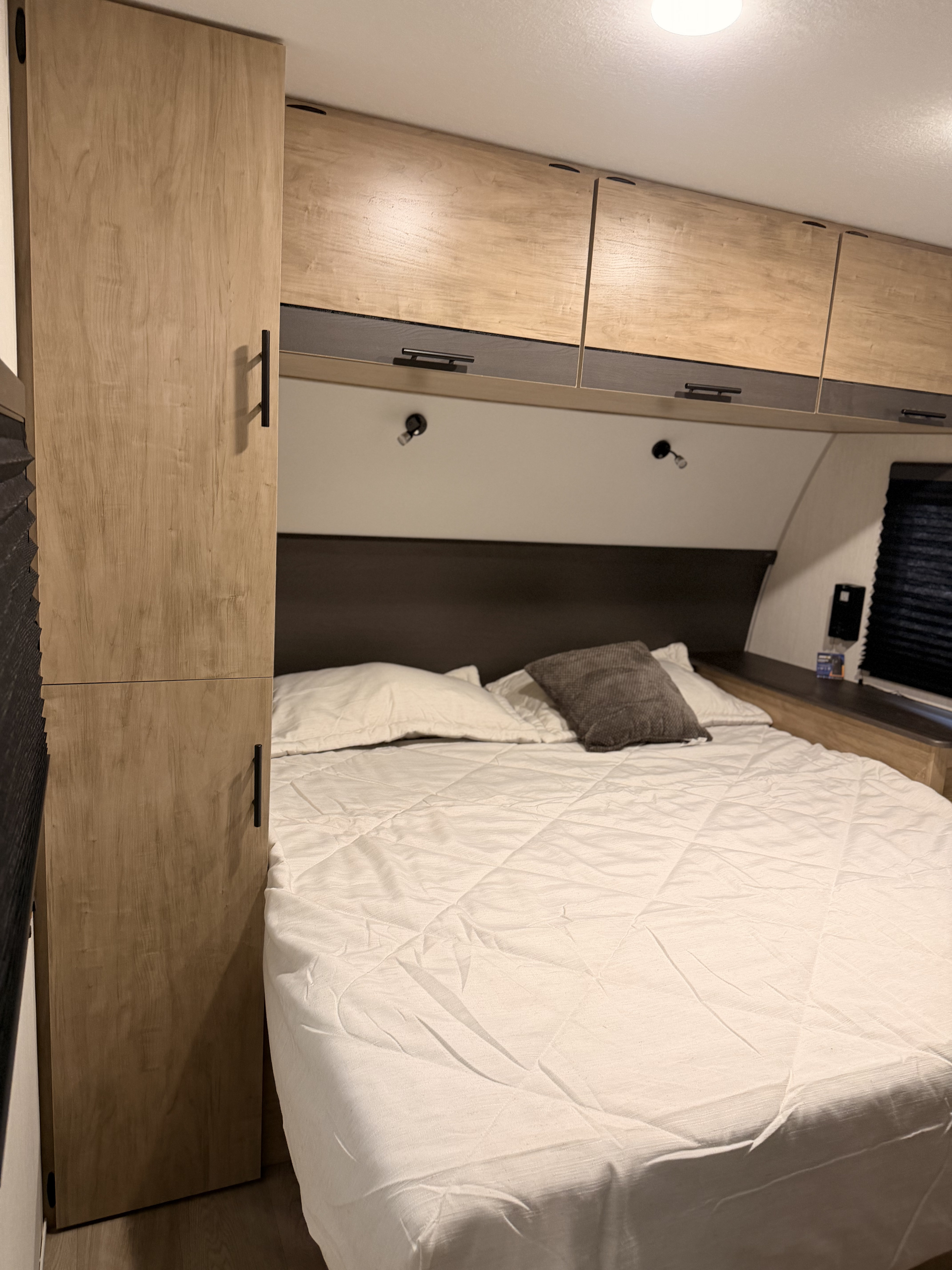 Cozy RV rental bedroom features light wood cabinets, a comfortable bed with white quilting, and reading lights above.. Forest River Campsite Reserve 2026