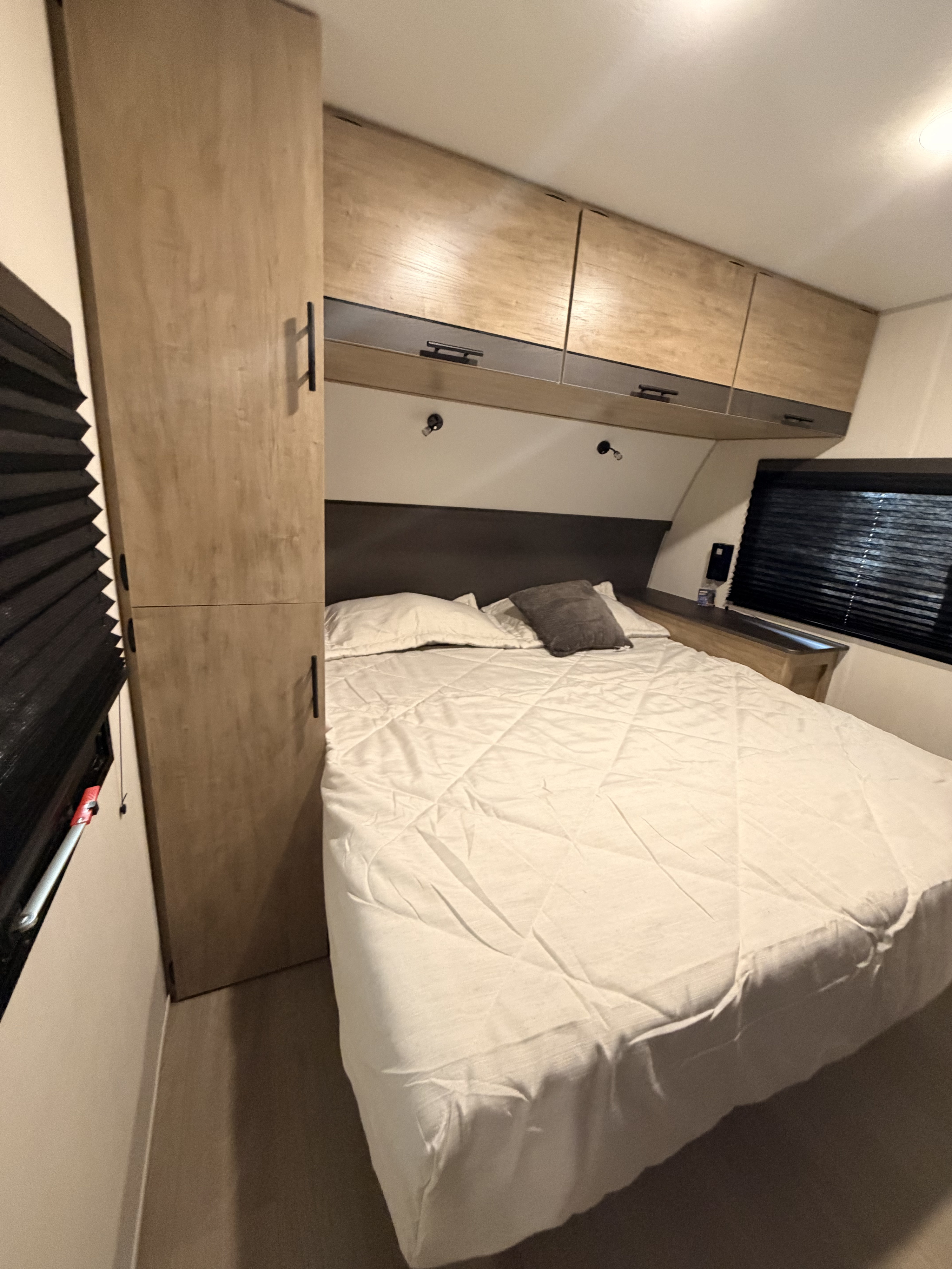 Neatly made bed with light bedding in a modern RV rental bedroom, featuring wooden cabinets, a wardrobe, and black blinds.. Forest River Campsite Reserve 2026