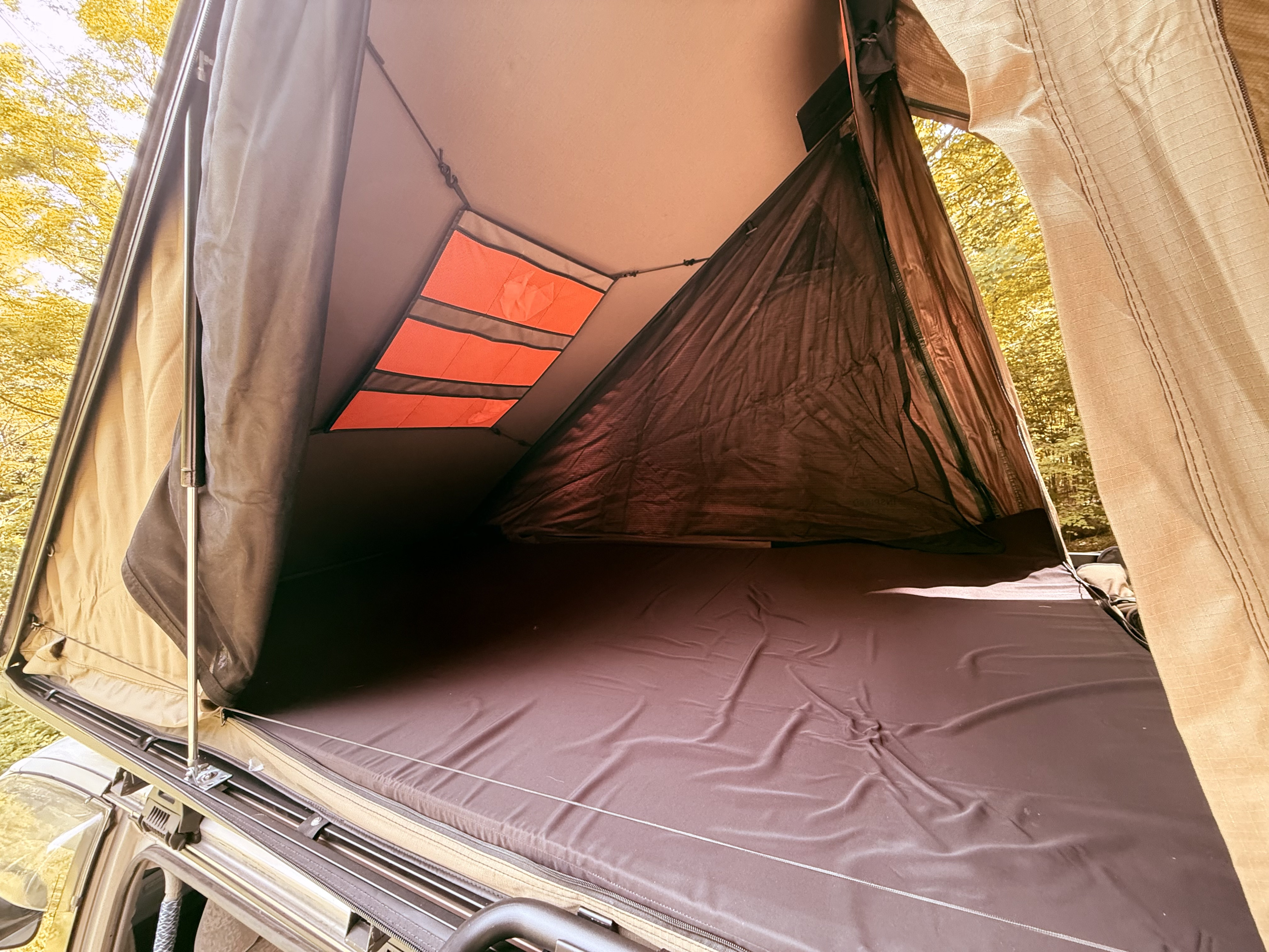 RV rental adventure: Comfy rooftop tent interior with dark mattress, storage pockets, and mesh panels overlooking the forest.. Mitsubishi Delicia 1996